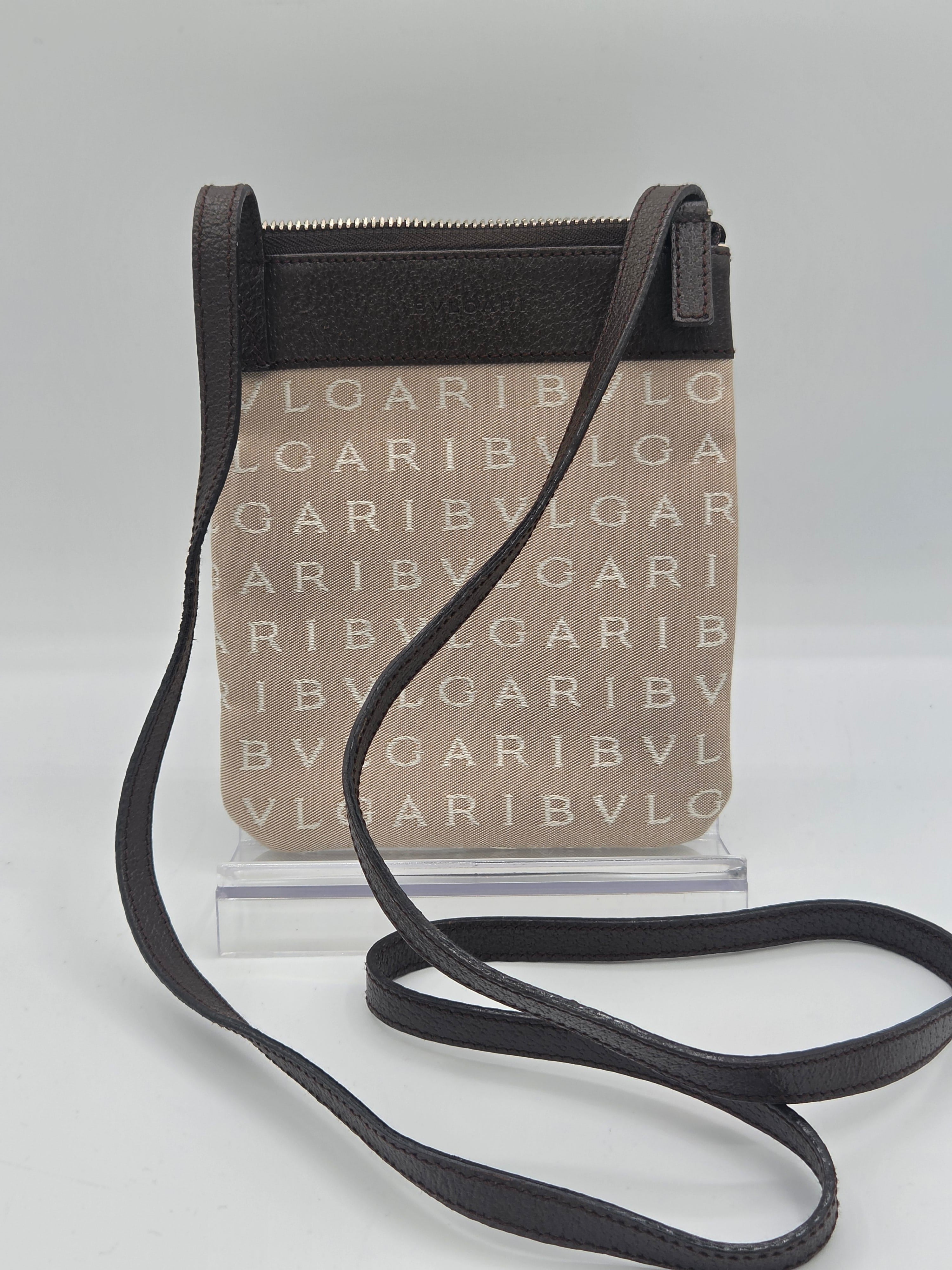 A black leather crossbody bag with a clear front pouch printed with repeating beige 'GARIBVL' text, shown on a light gray background.