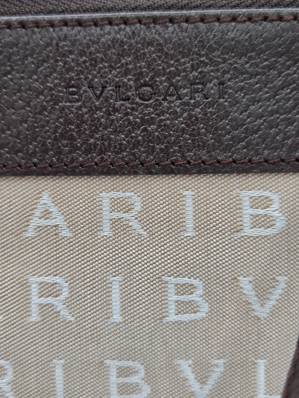 Close-up detail of a luxury wallet or card case featuring a dark brown textured leather panel with debossed 'BVL' branding and a beige canvas section with repeating light gray 'ARIB V.
