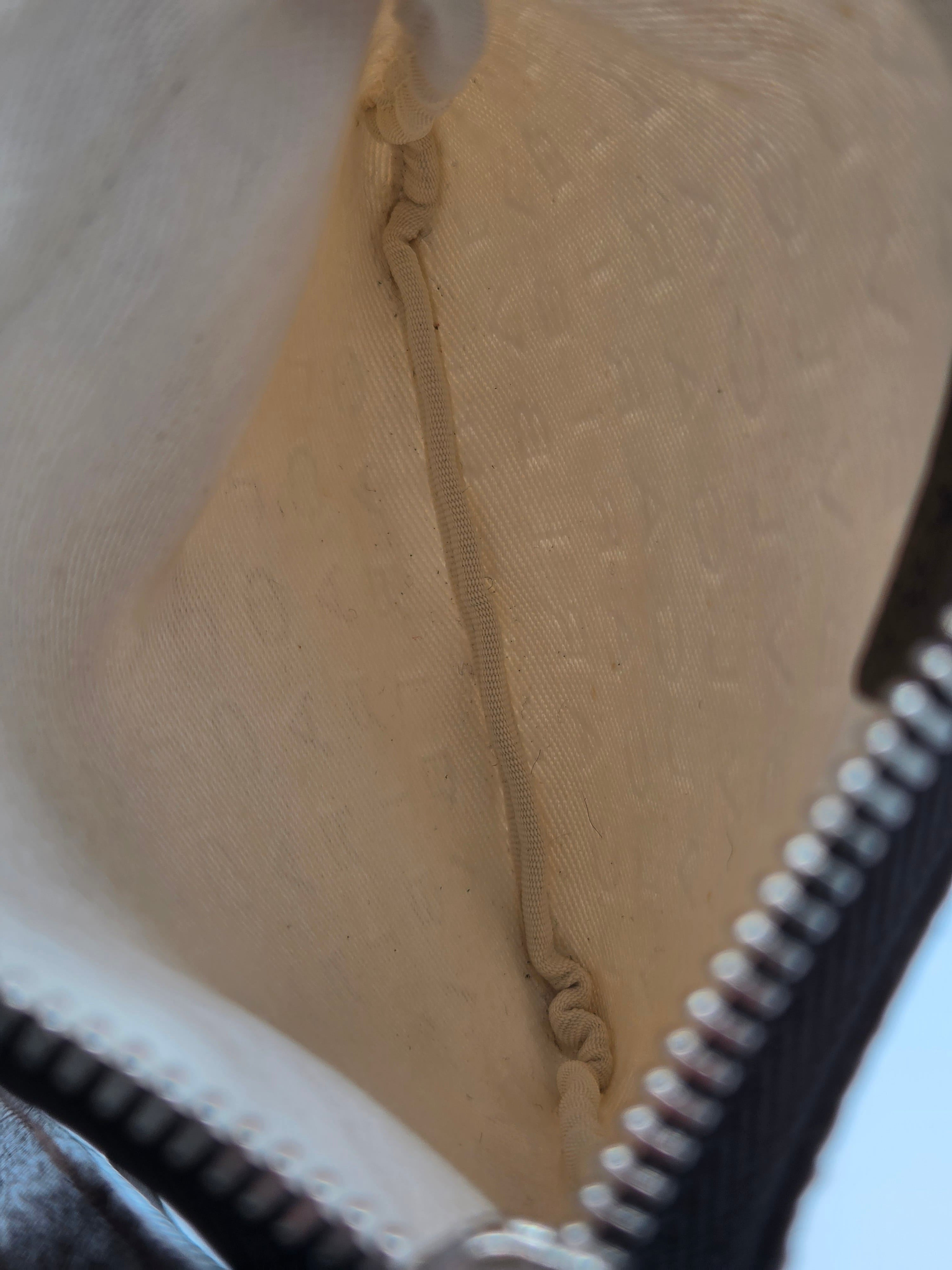 Close-up of the interior of a beige monogrammed bag, showing a tan elastic band and a black zipper with silver metal teeth.