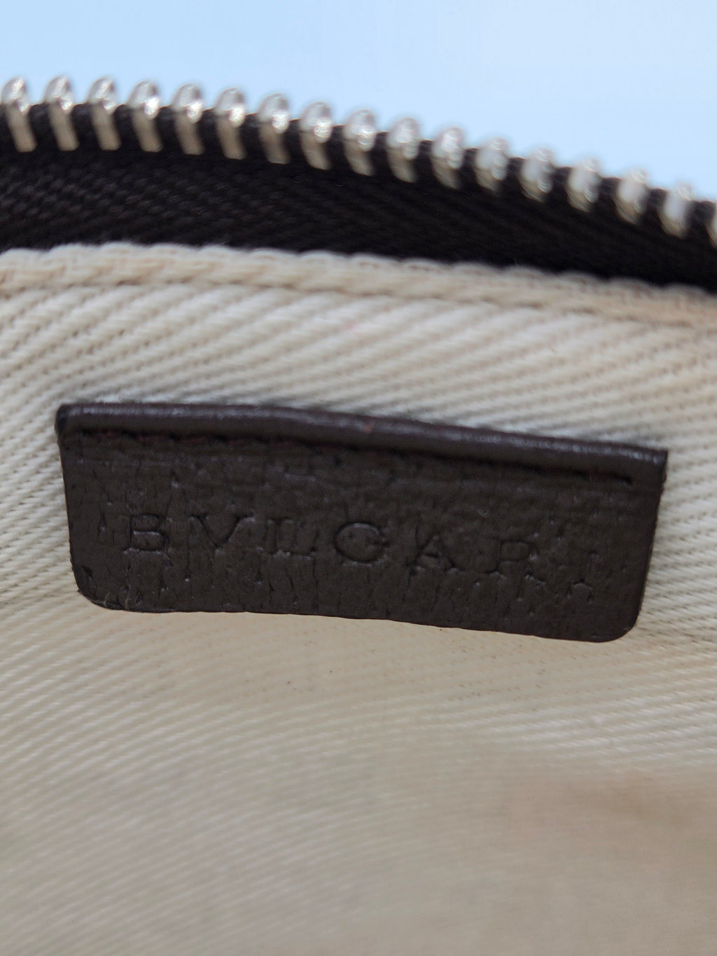 Close-up of a beige canvas bag with a black leather patch embossed with the brand name 'BYUCKAR' next to a black zipper.