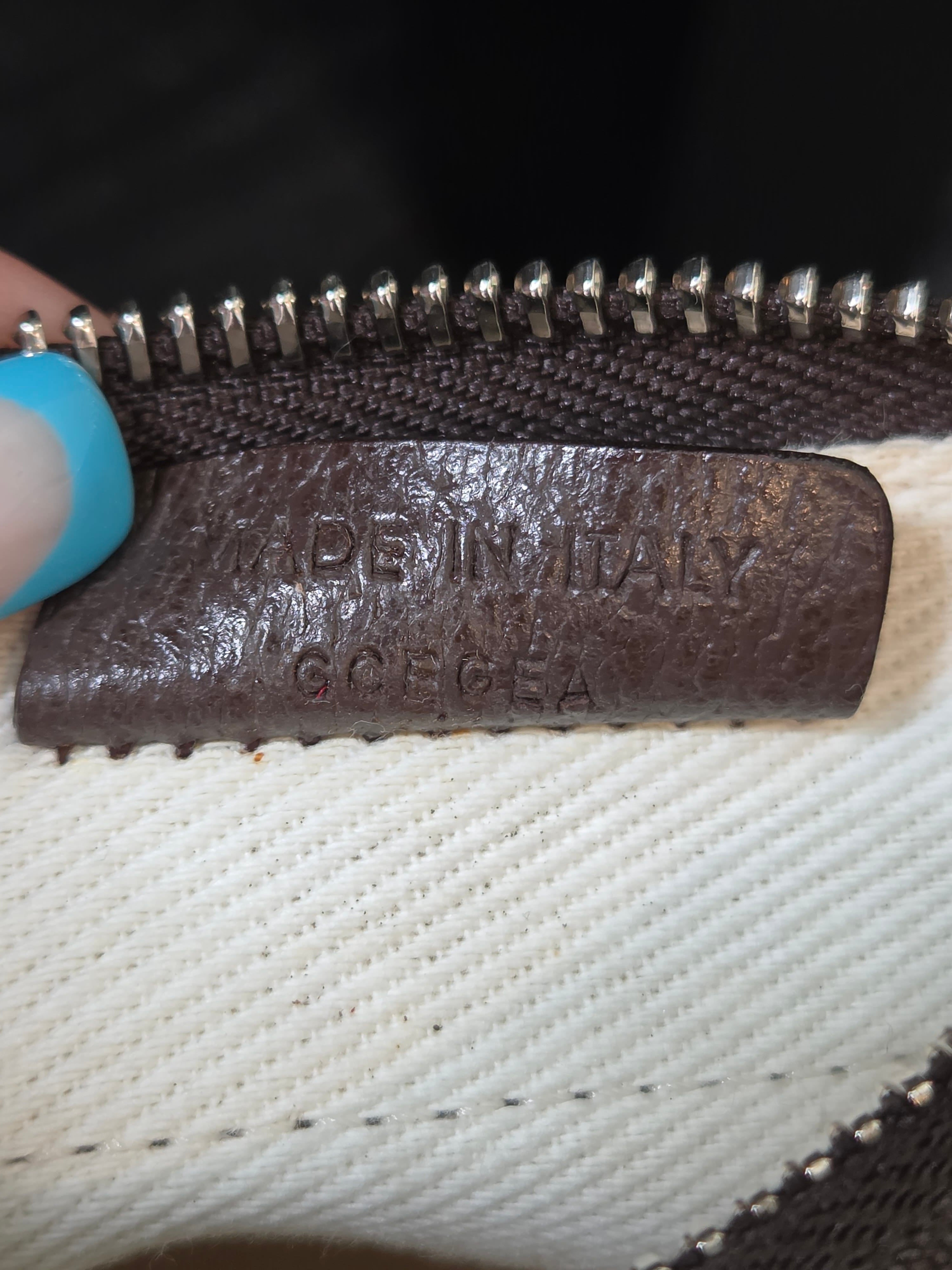 Close-up of a dark brown leather zipper pull tab with embossed text reading 'Made in Italy, S.Cecca' next to a white woven textile and silver zipper teeth.