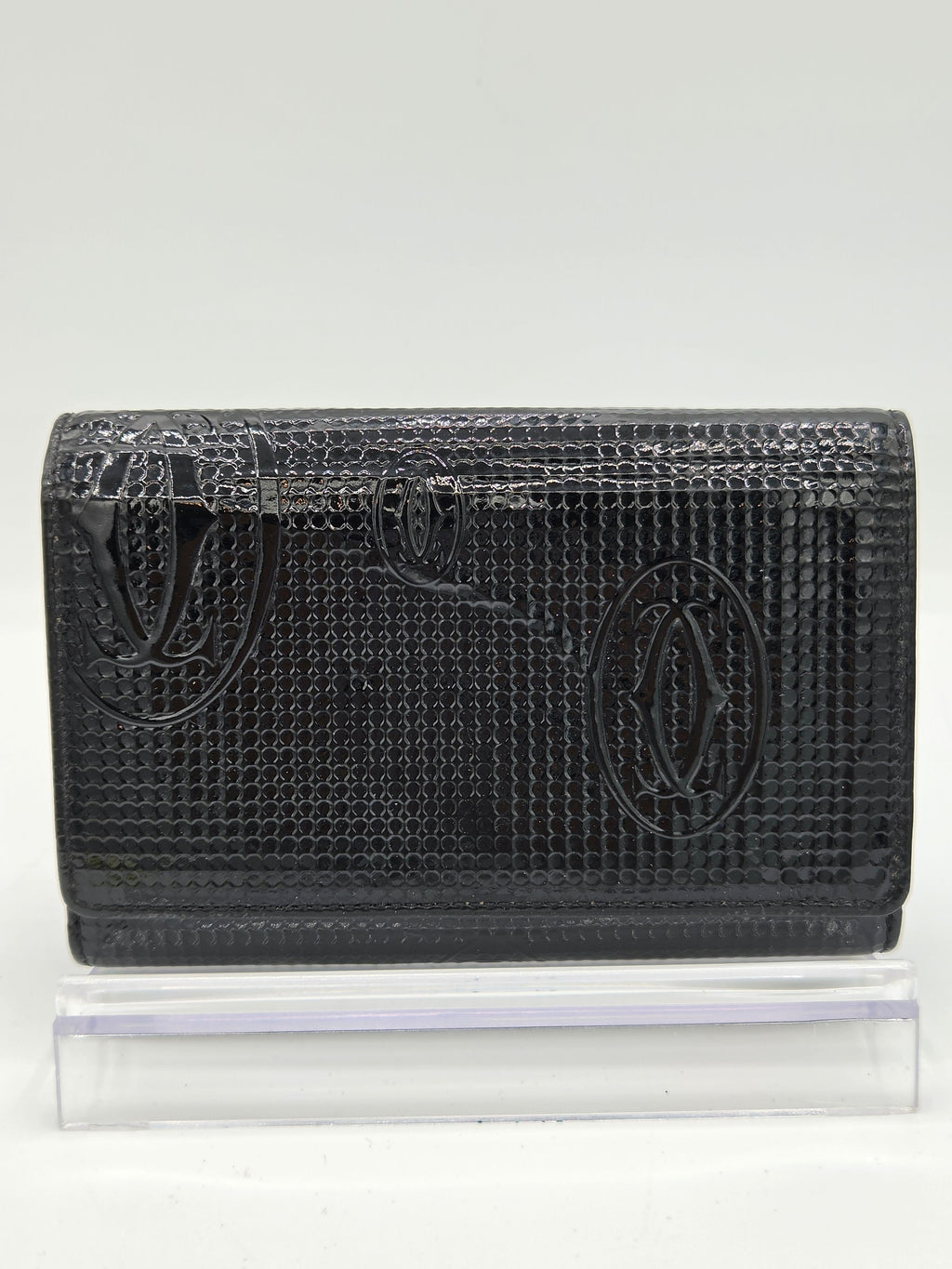 A black textured leather wallet with an embossed fish logo, shown next to a clear plastic protective sleeve on a white background.