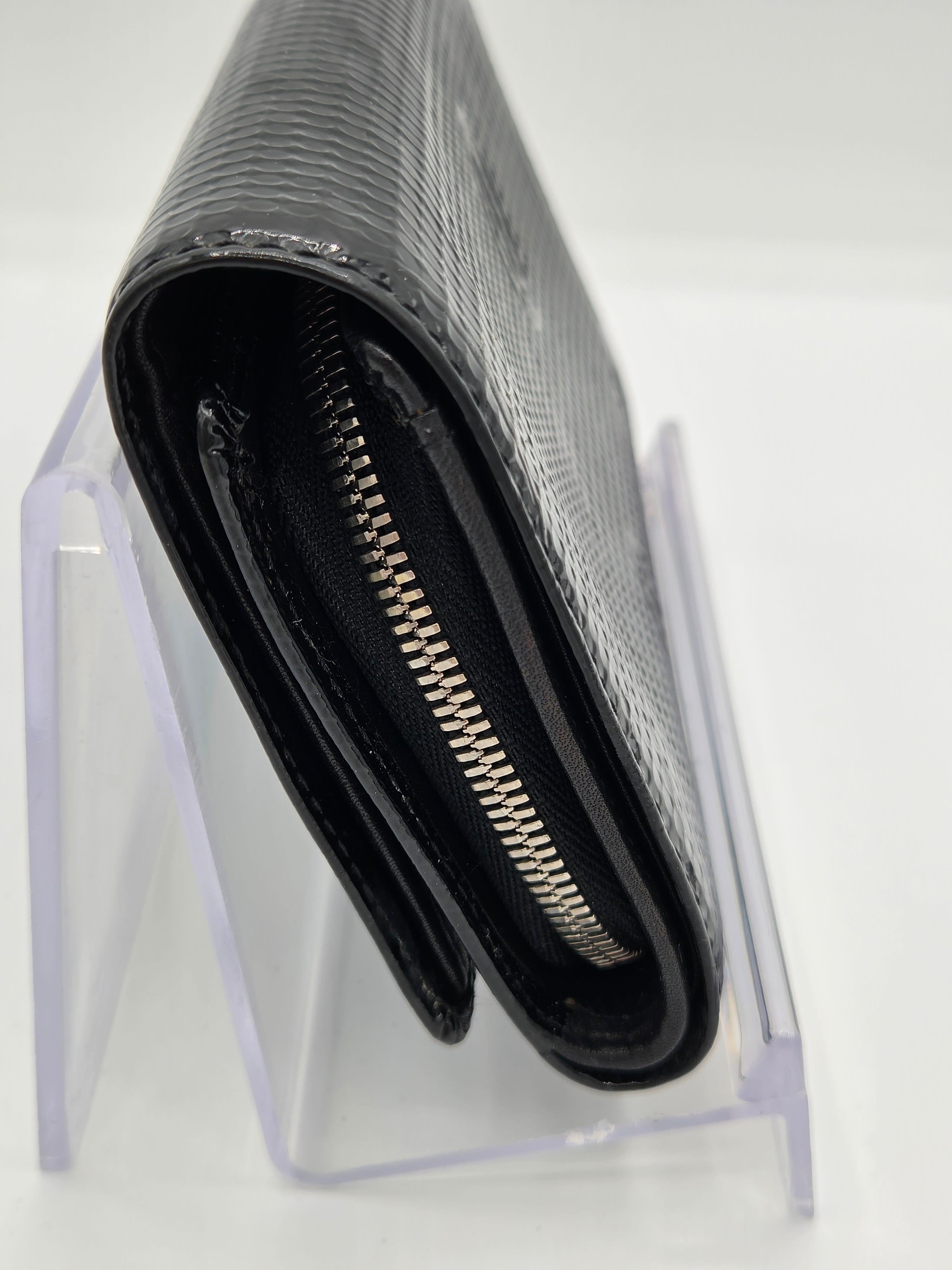 A black textured leather zip-around wallet resting on a clear acrylic display stand against a white background.