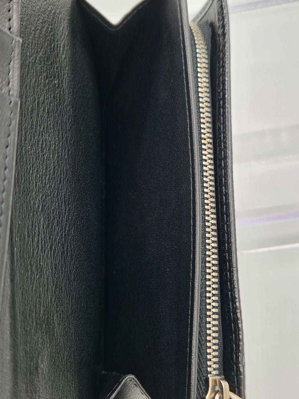 Close-up of the interior of a black leather clutch or wallet, showing the black textured leather lining and a silver-toned metal zipper.