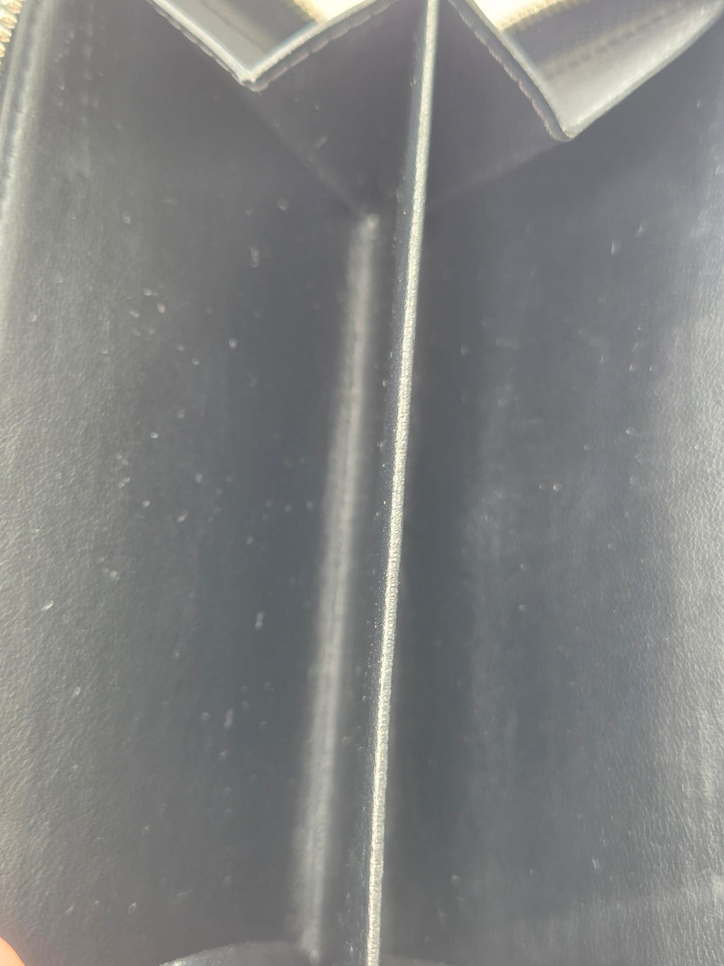 Close-up of a black textured leather or faux-leather compartment, showing a horizontal divider and a vertical side tab with visible lint and dust specks.