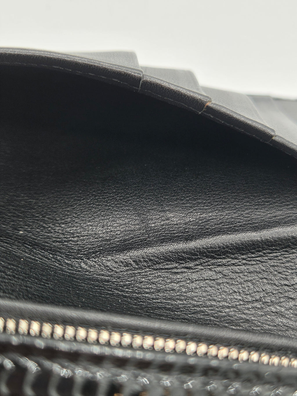 Close-up detail of a black textured leather zipper pouch or bag, showing the pebbled leather texture, black stitching, and a gold-toned metal zipper.