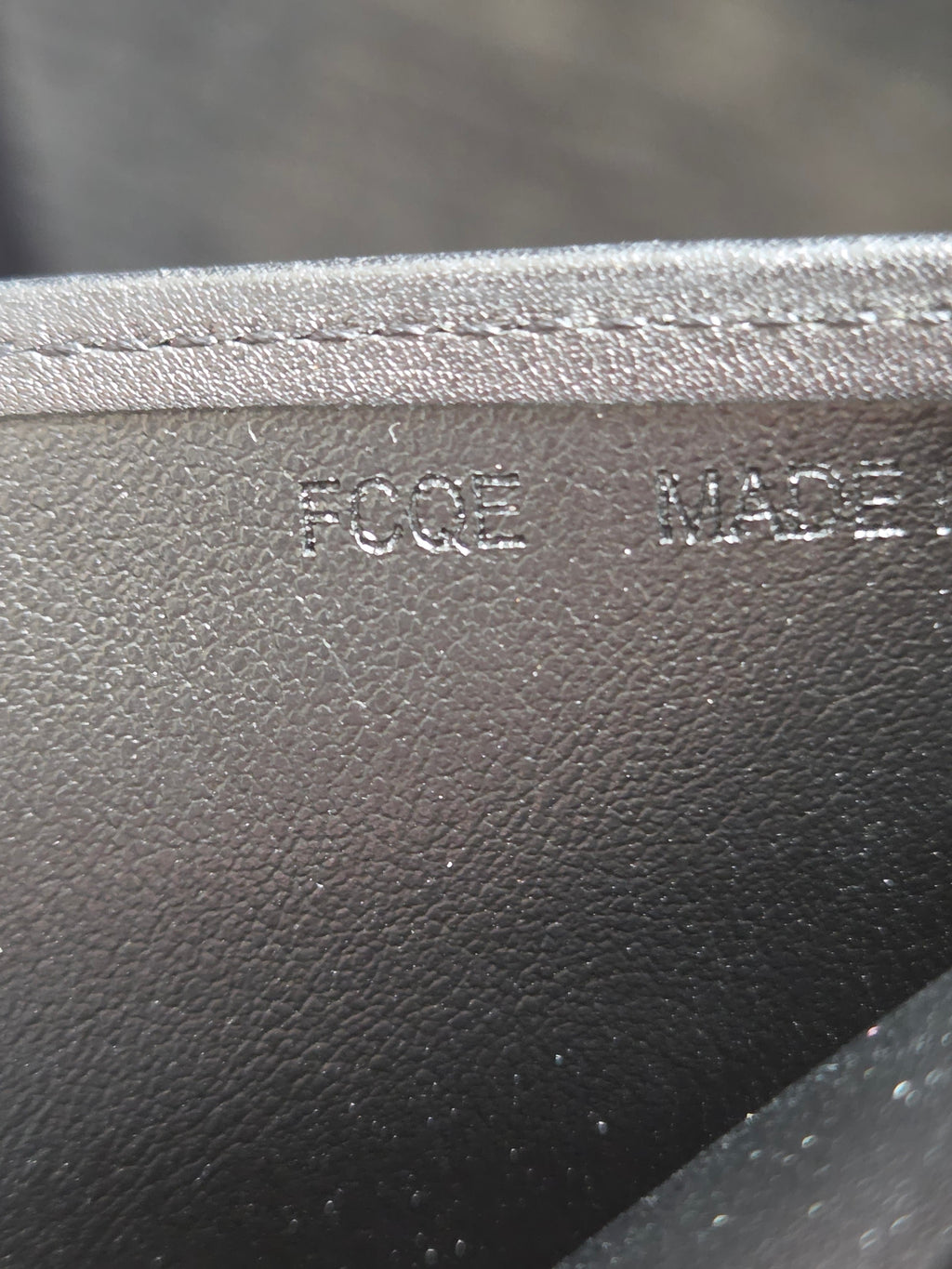 Close-up of a black pebbled leather or faux-leather material with a stitched edge and embossed vertical text reading 'FOGE MADE'.