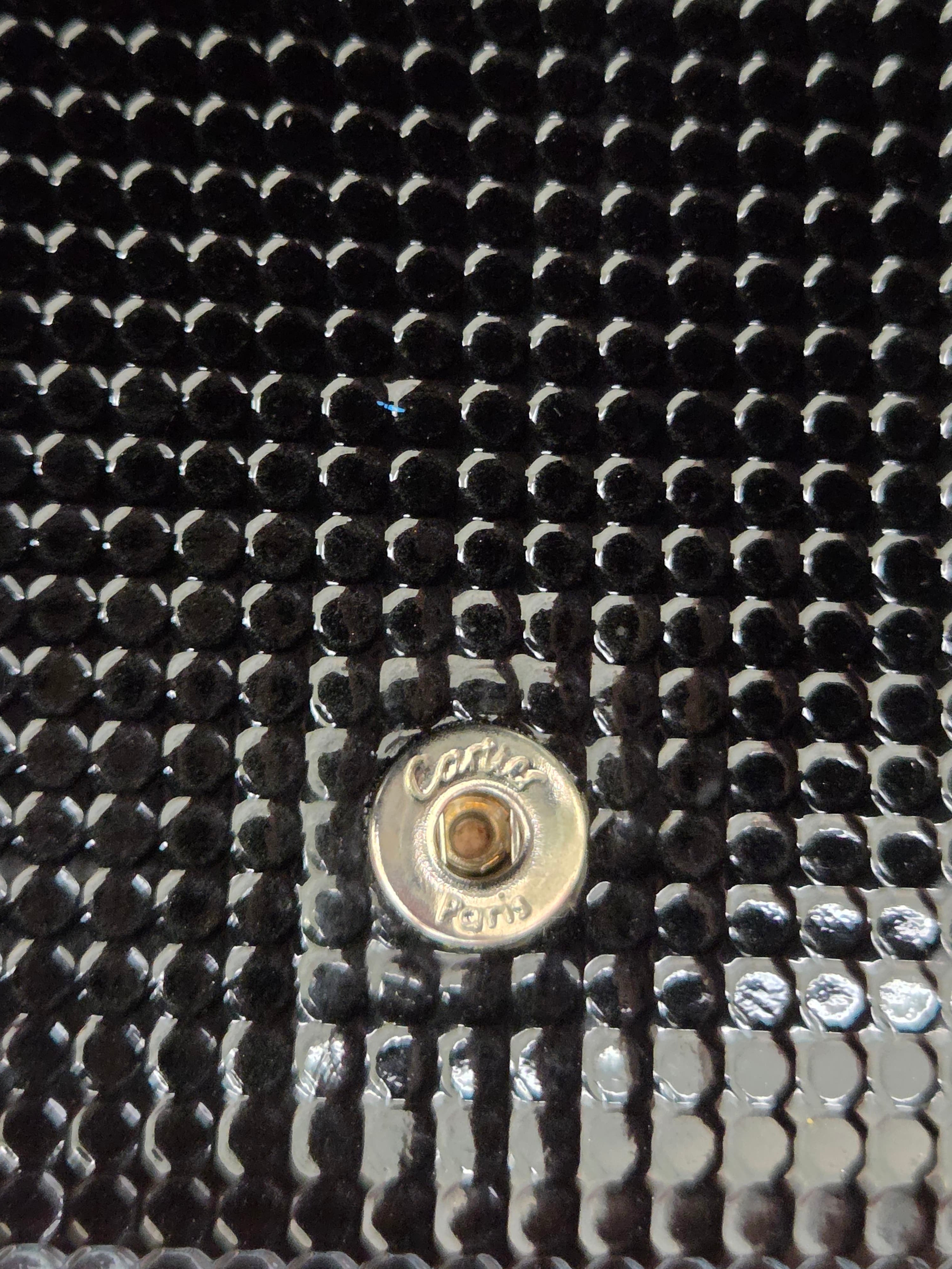 Close-up of a black textured surface with a circular metallic button or rivet in the center, showing engraved text that appears to read 'Cavelli Paris'.