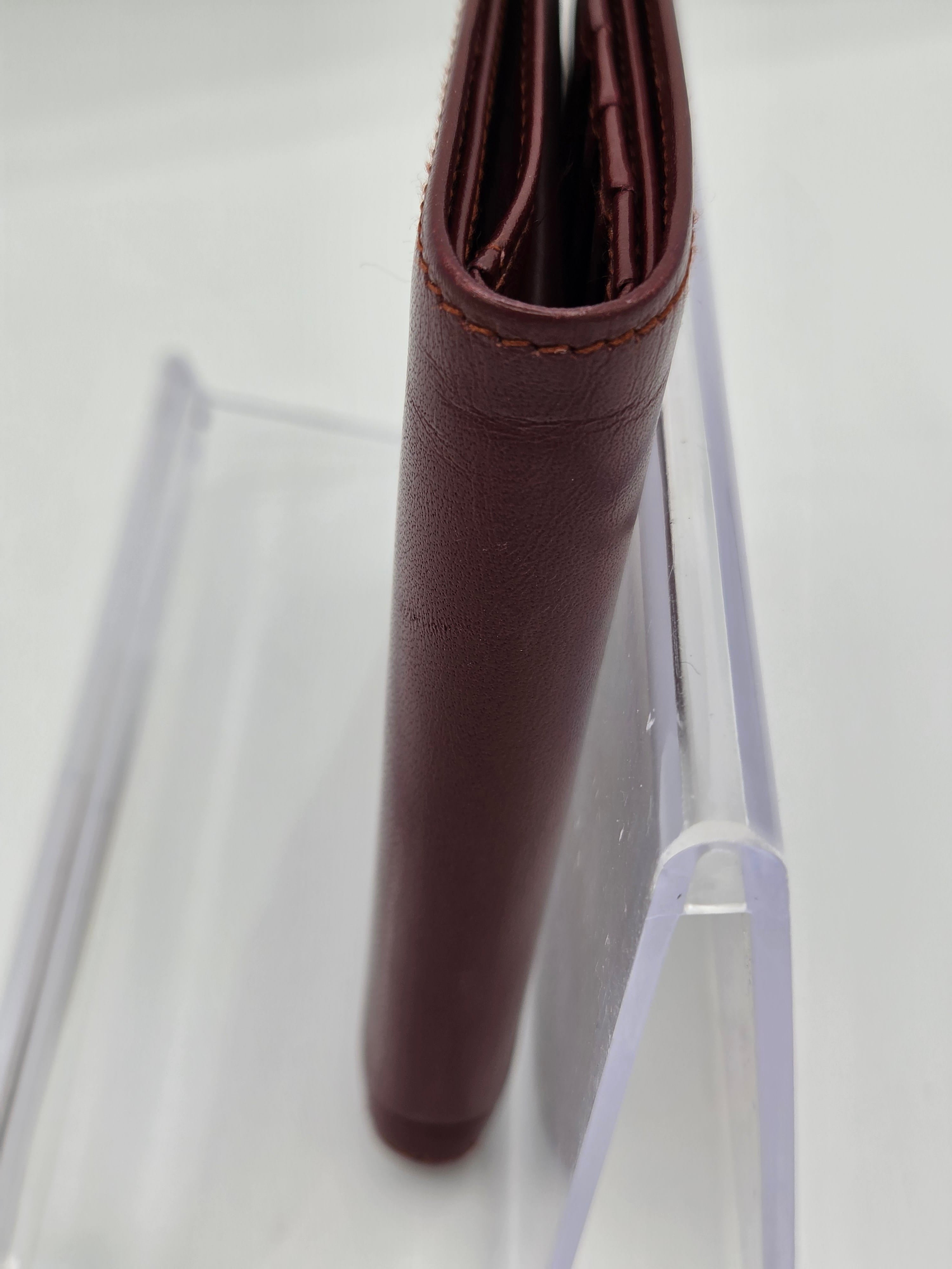 A close-up of a dark reddish-brown leather wallet standing upright in a clear acrylic display stand against a white background.