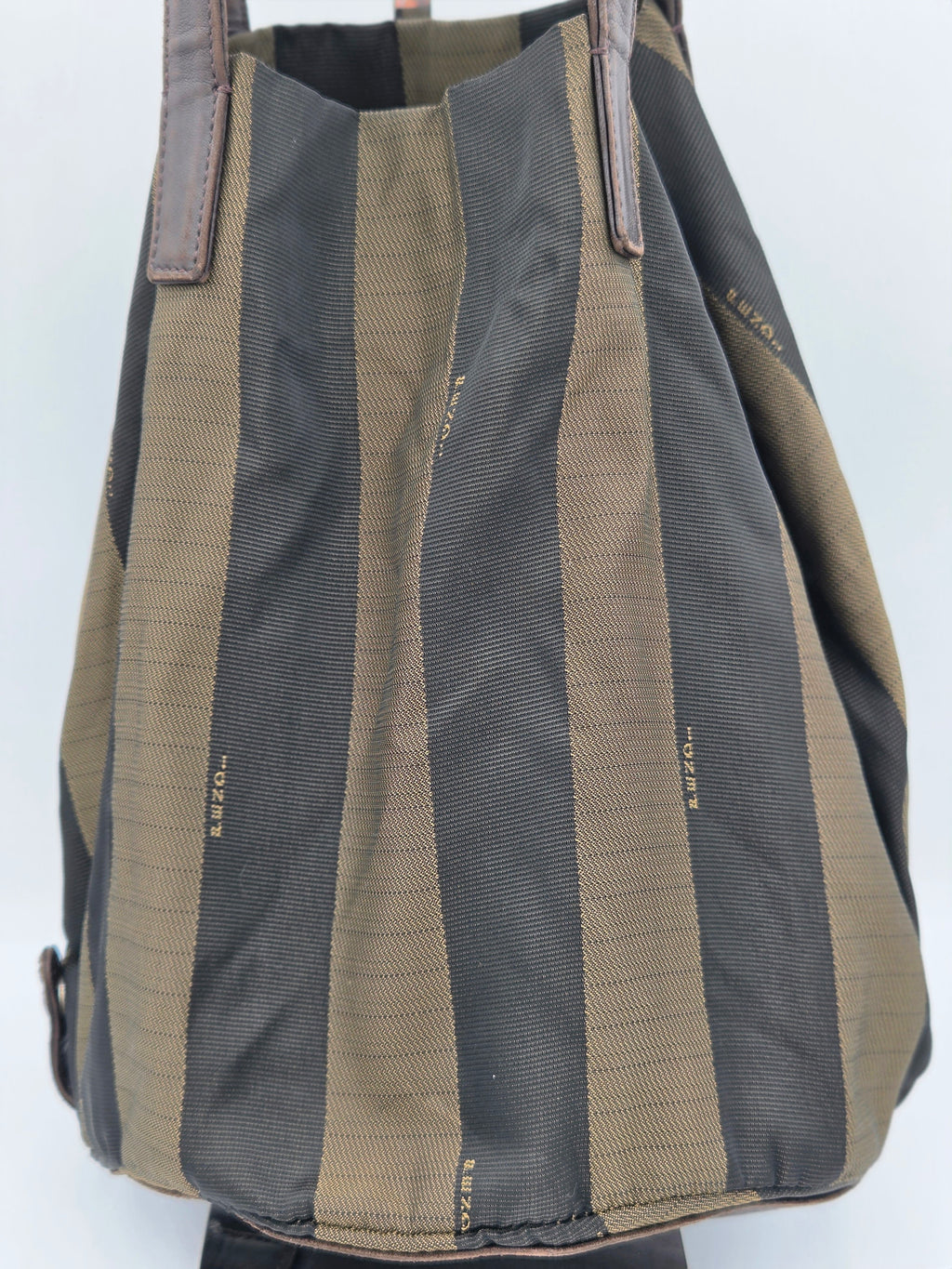 A canvas tote bag with vertical stripes in olive green and dark gray, featuring brown leather handles and subtle gold brand lettering.