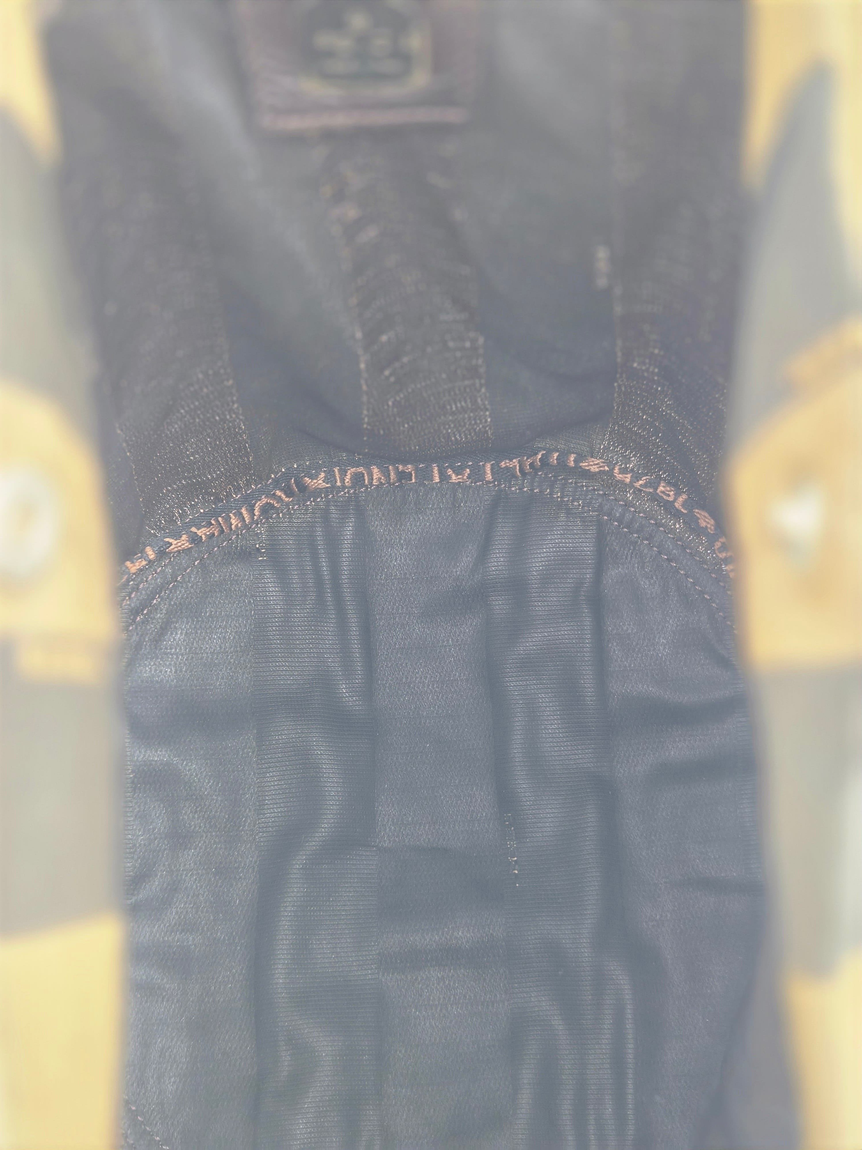 Close-up of a dark charcoal gray or black textured fabric garment, showing a gathered waistband with orange-brown contrast stitching and a small embroidered brand patch at the top.
