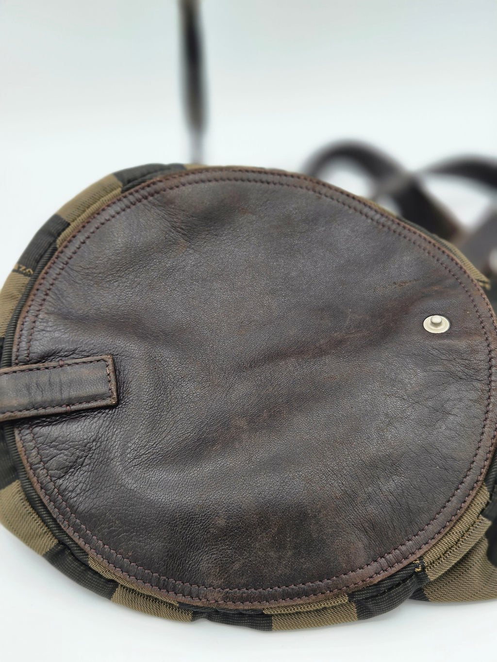 Close-up of a round brown leather pouch or cover with visible stitching, a small metal rivet, and a camouflage-patterned edge trim on a white background.