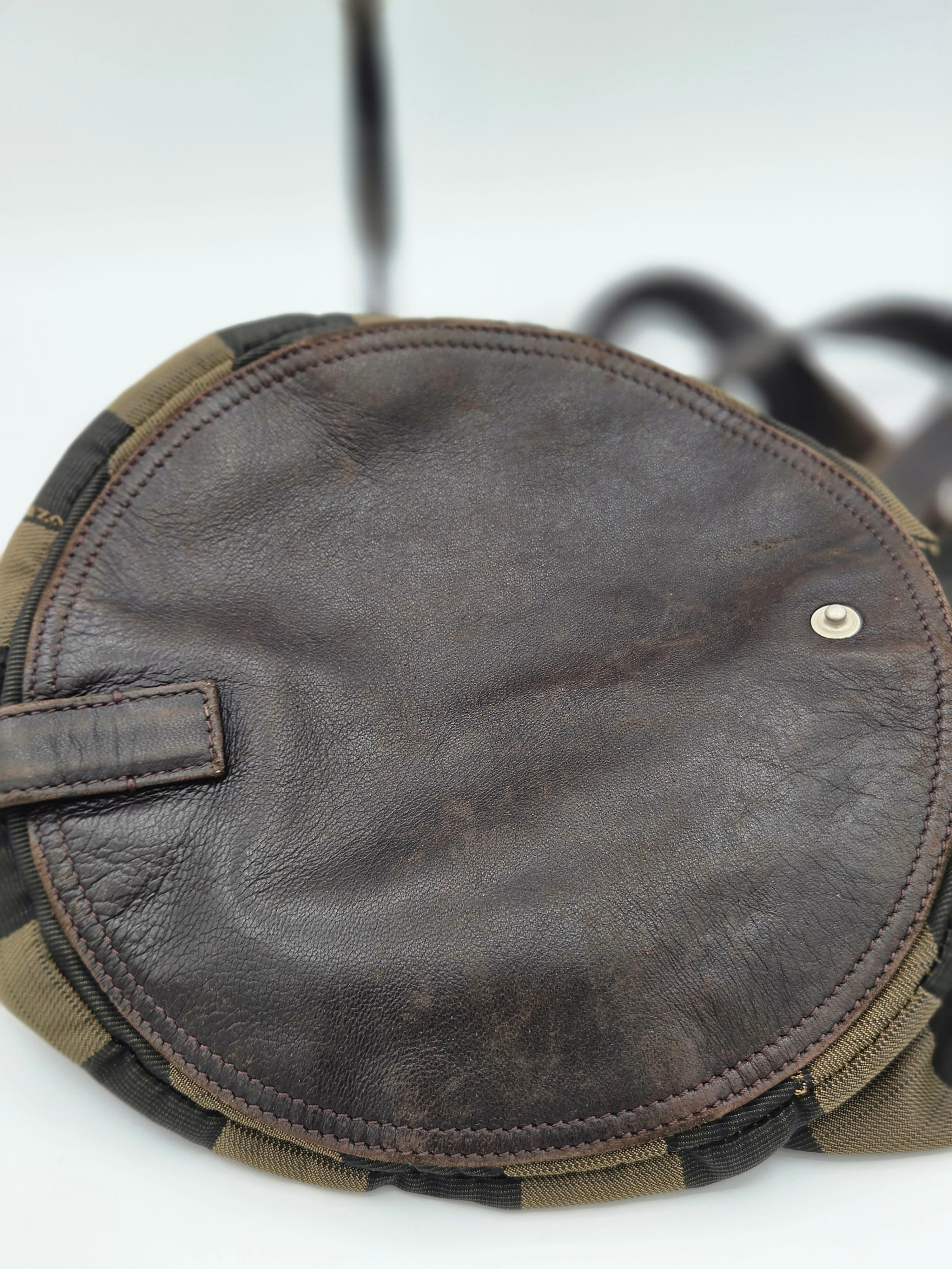 Close-up of a round brown leather pouch or cover with visible stitching, a small metal rivet, and a camouflage-patterned edge trim on a white background.