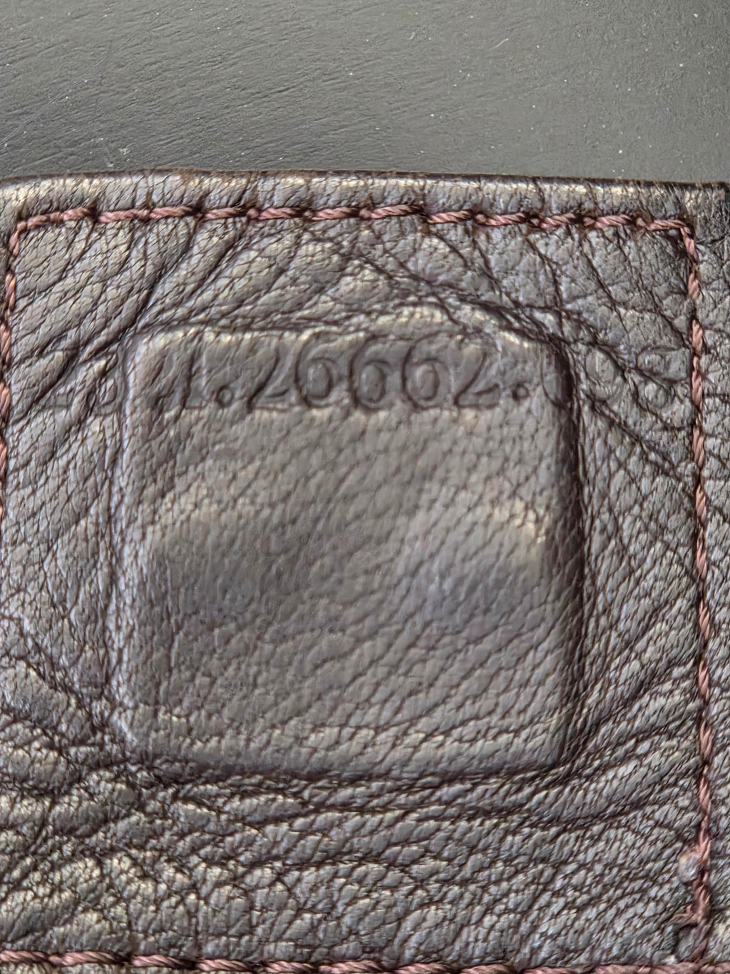 Close-up of a dark brown textured leather item, showing a stitched border and embossed vertical numbering.