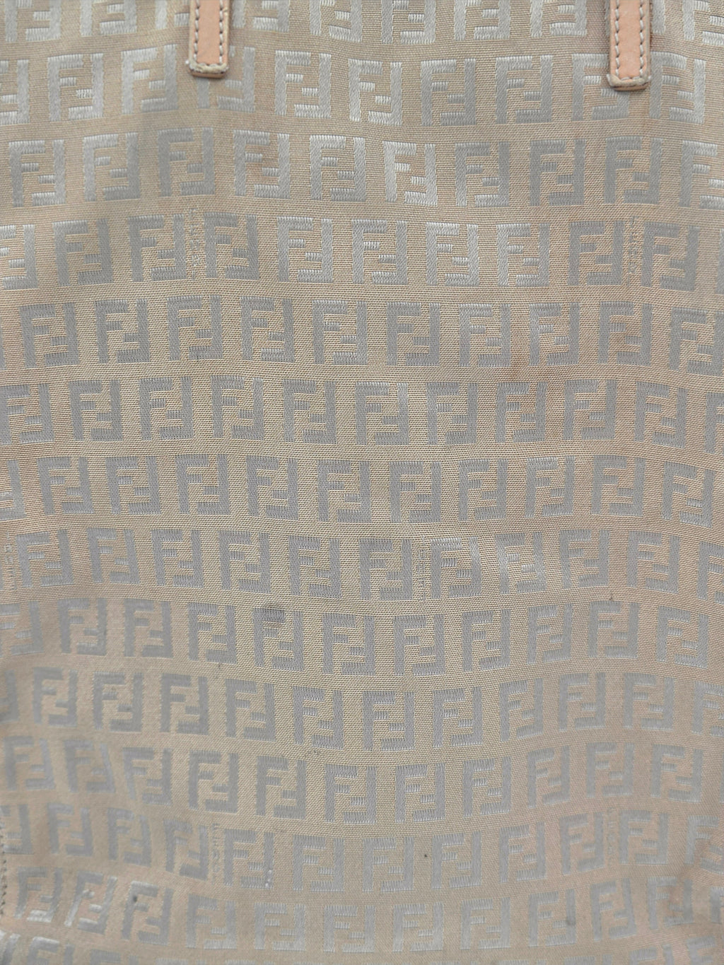 Close-up of a beige fabric with a repeating light gray geometric monogram pattern and small tan leather tab details at the top.
