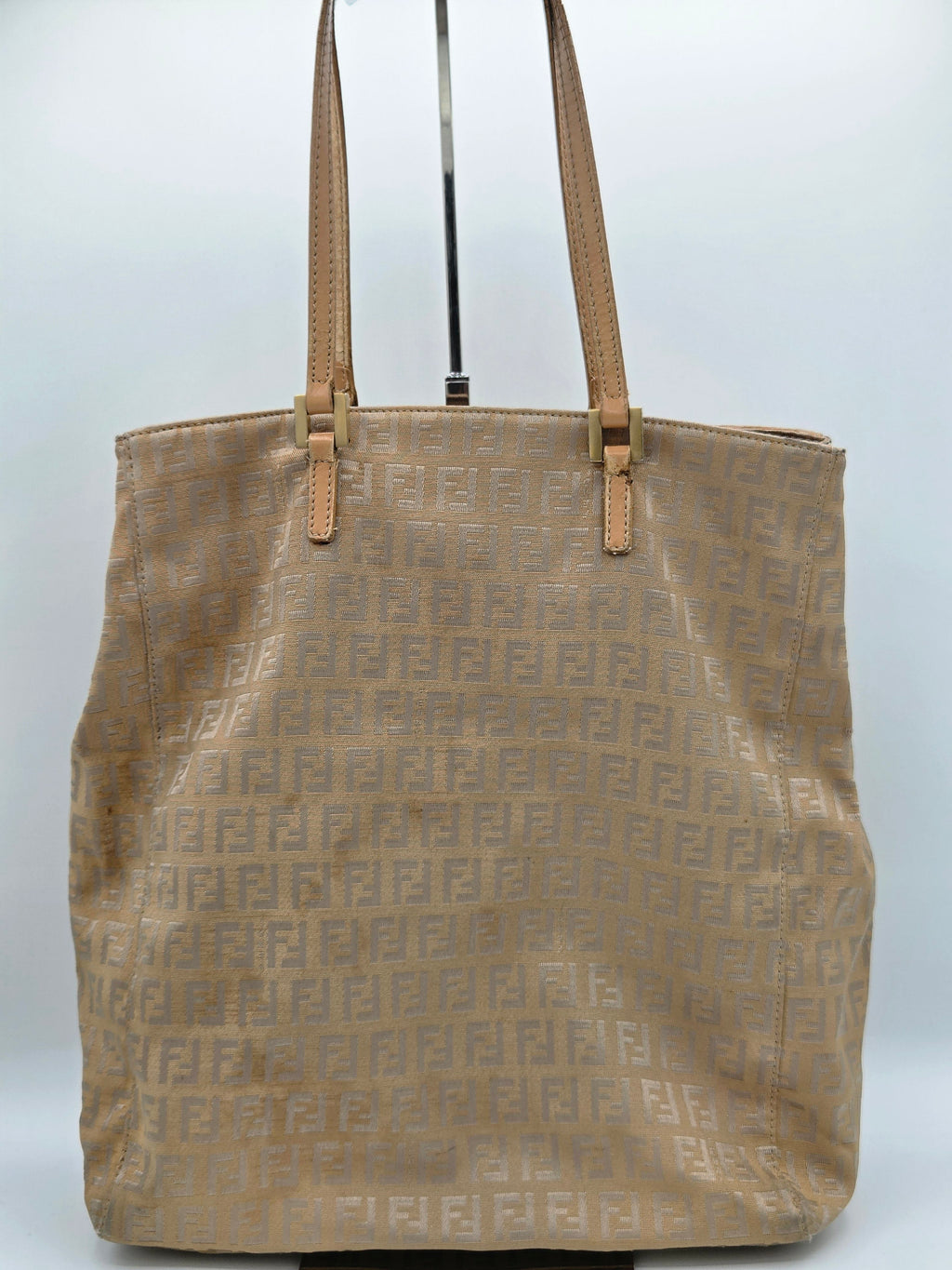 A beige Fendi tote bag with an all-over embossed FF monogram pattern and tan leather shoulder straps, shown hanging against a plain light gray background.