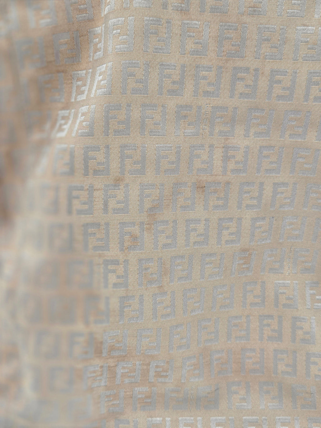 Close-up of a beige fabric with a repeating light gray geometric monogram pattern.