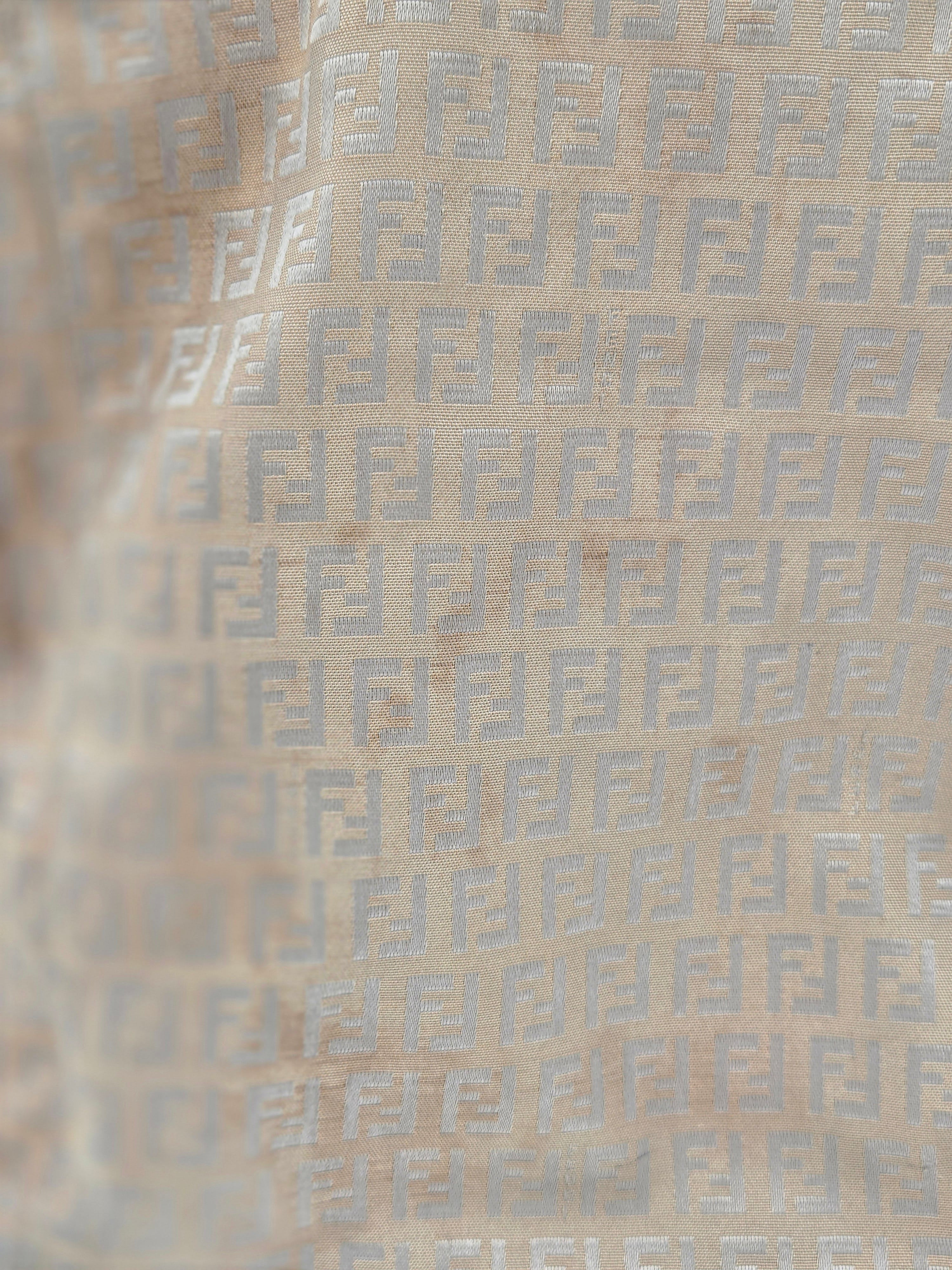 Close-up of a beige fabric with a repeating light gray geometric monogram pattern.