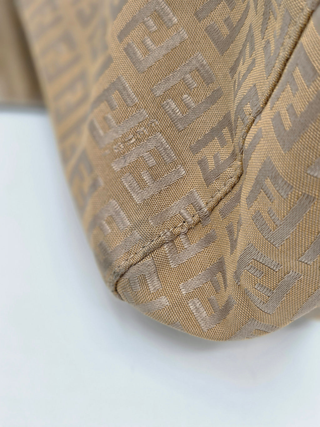 Close-up of a beige Fendi bag with the signature Zucca monogram pattern, showing the woven fabric texture and stitching.