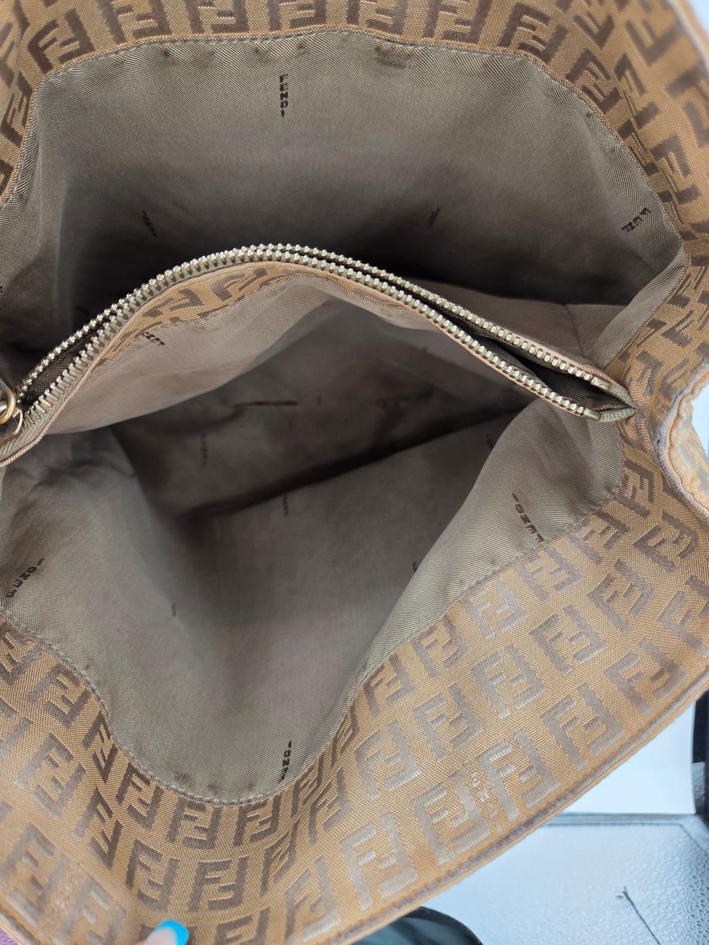 Close-up view of the interior of a Fendi handbag, showing the brown and beige Zucca monogram canvas lining and a gold-tone zipper.