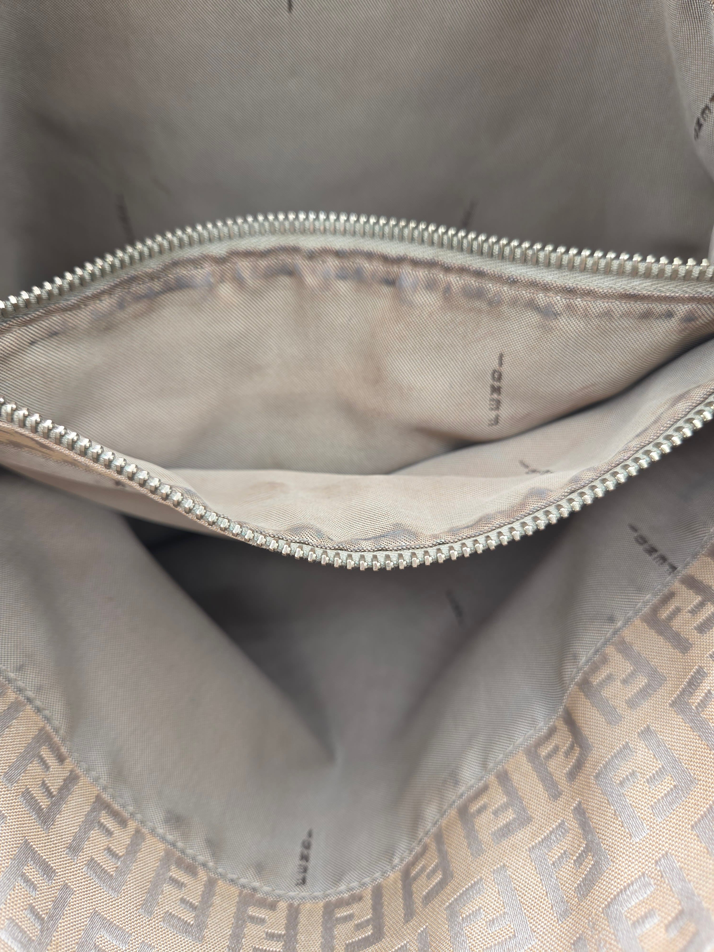 Close-up of the interior of a beige Fendi bag with a silver zipper and the signature Zucca monogram pattern visible along the bottom edge.