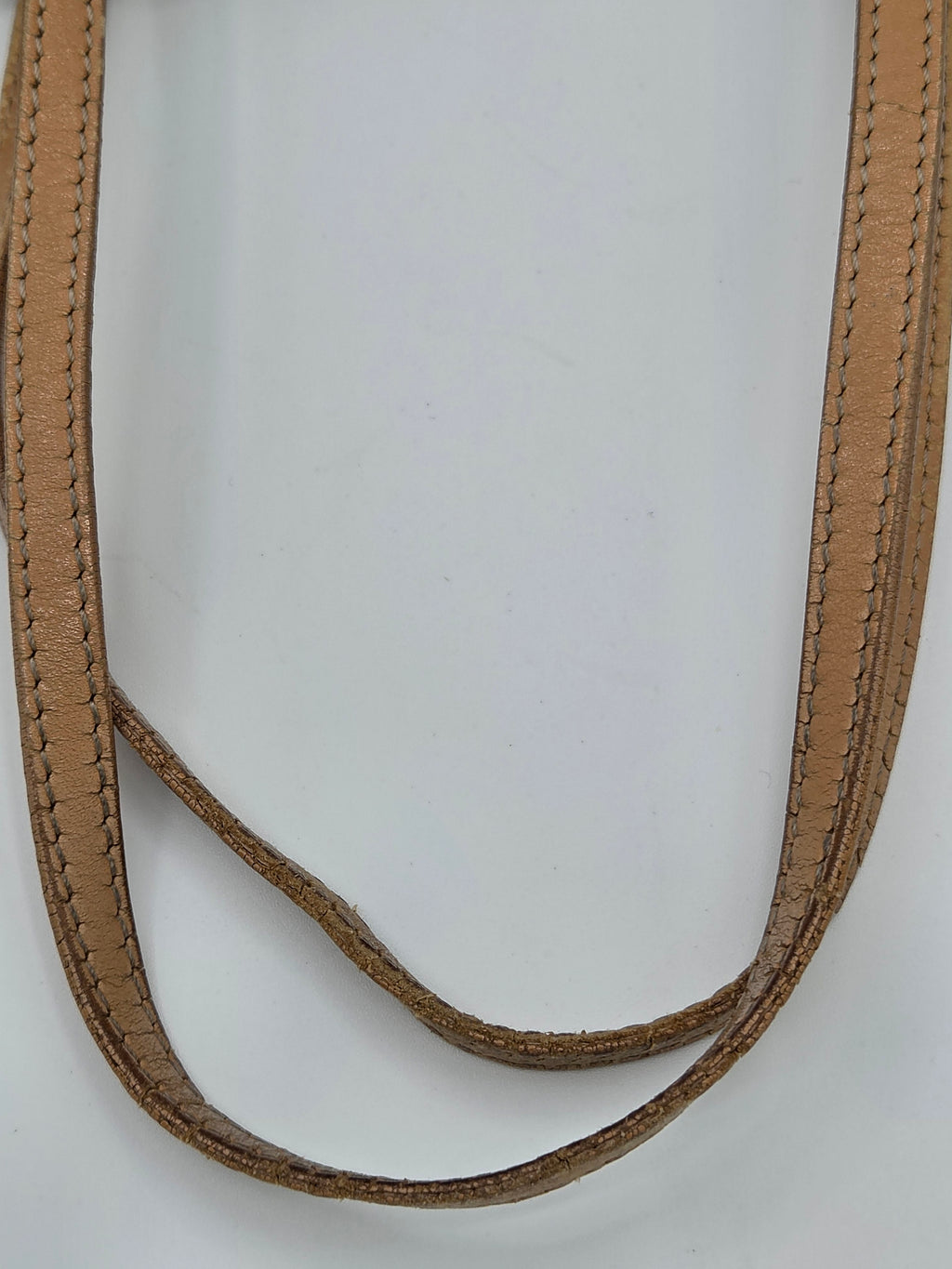 A close-up of a tan leather strap with double rows of matching stitching, arranged in a loop on a plain white background.
