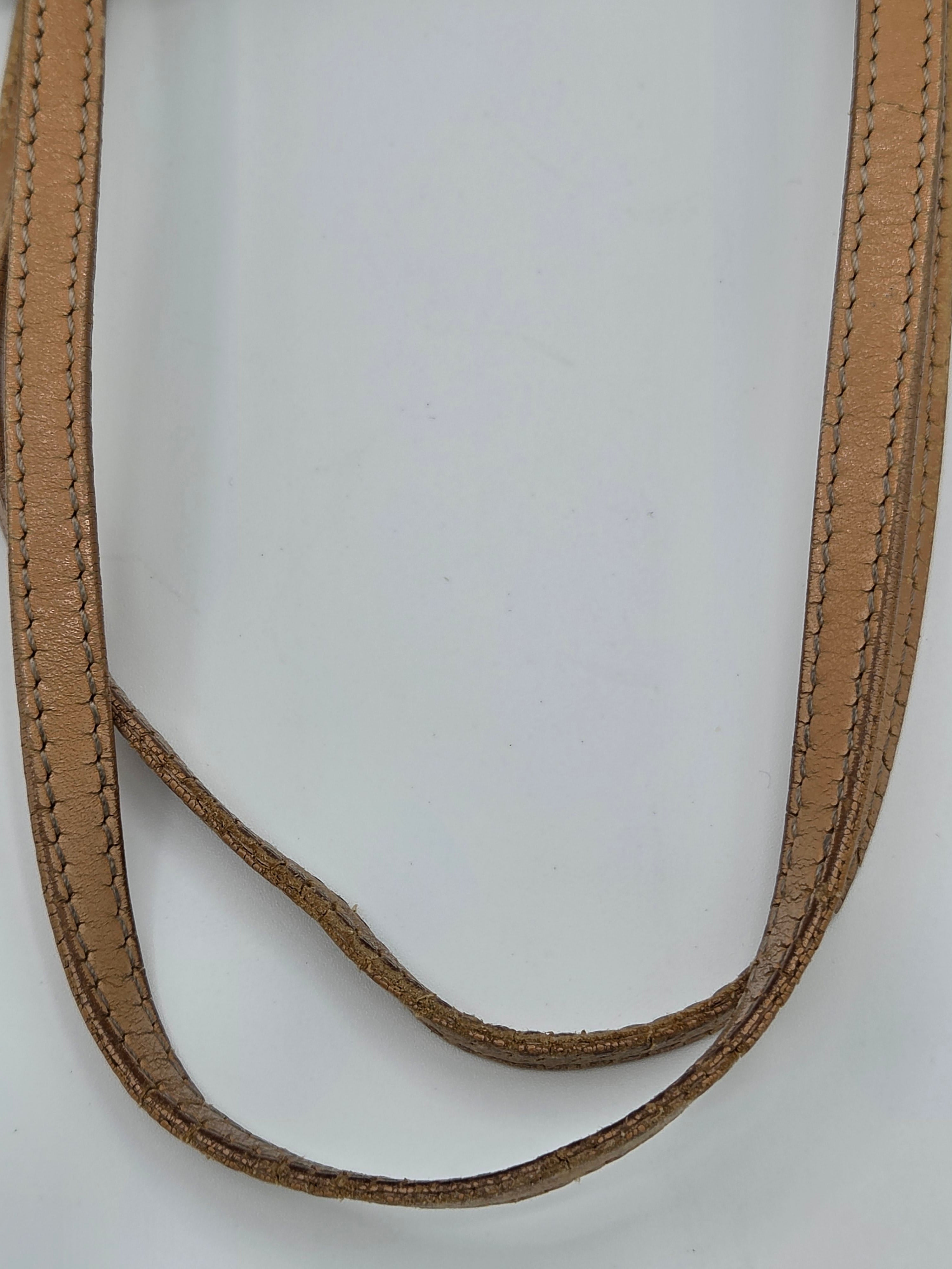 A close-up of a tan leather strap with double rows of matching stitching, arranged in a loop on a plain white background.