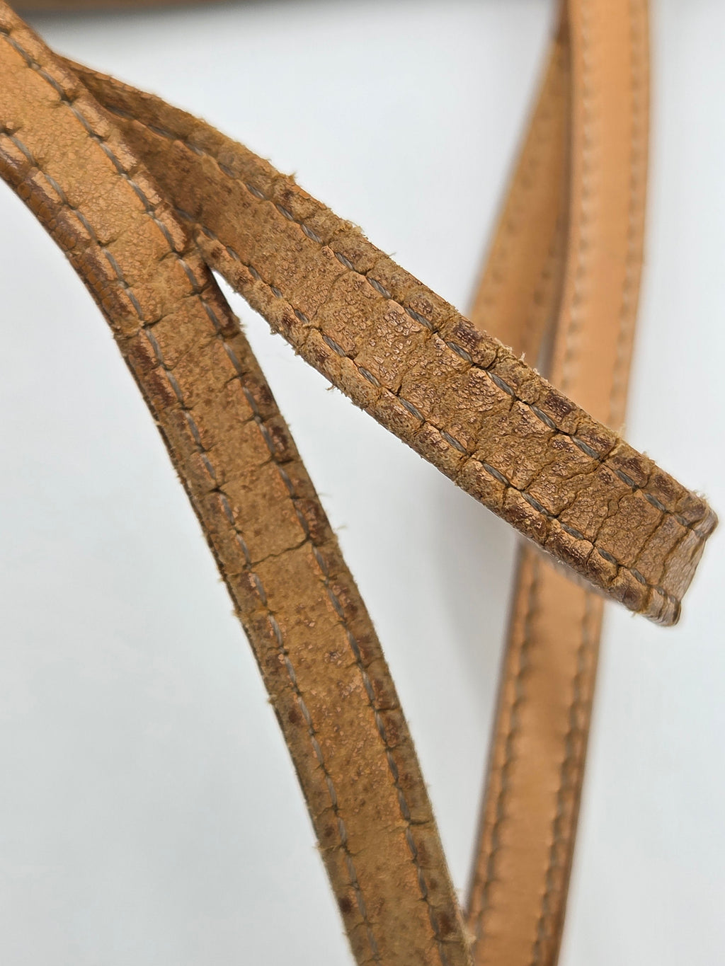 A close-up of a tan leather strap with visible texture and stitching, set against a plain light gray background.