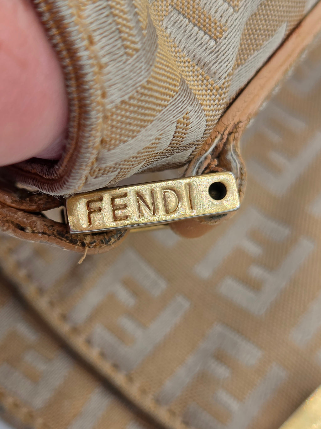 Close-up of a Fendi monogrammed beige and white canvas bag with a gold-tone metal zipper pull engraved with the Fendi logo.