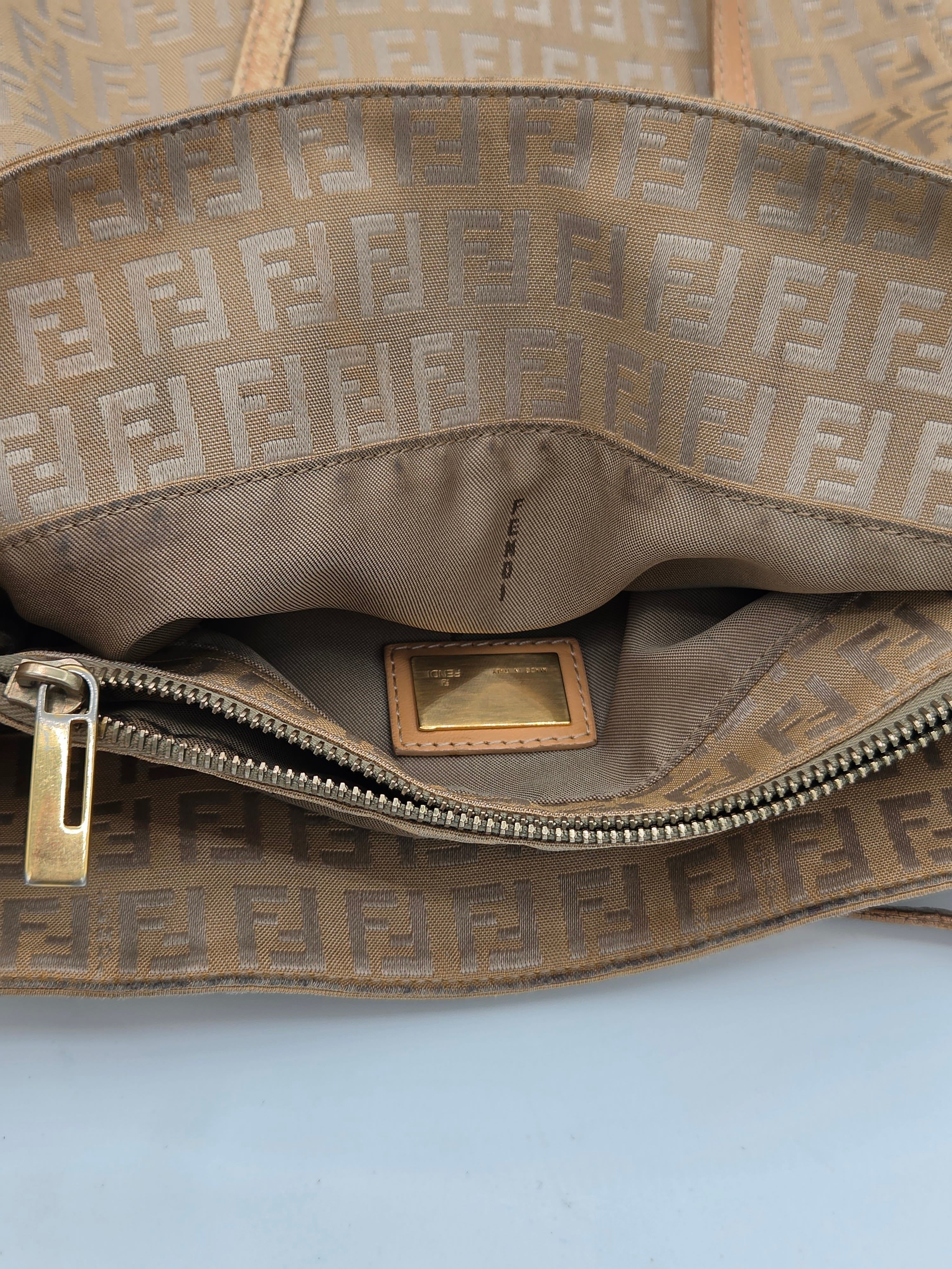 Close-up of a Fendi bag interior showing the signature brown and beige FF monogram canvas exterior, tan interior lining, a gold-tone zipper pull, and a small interior brand plaque.