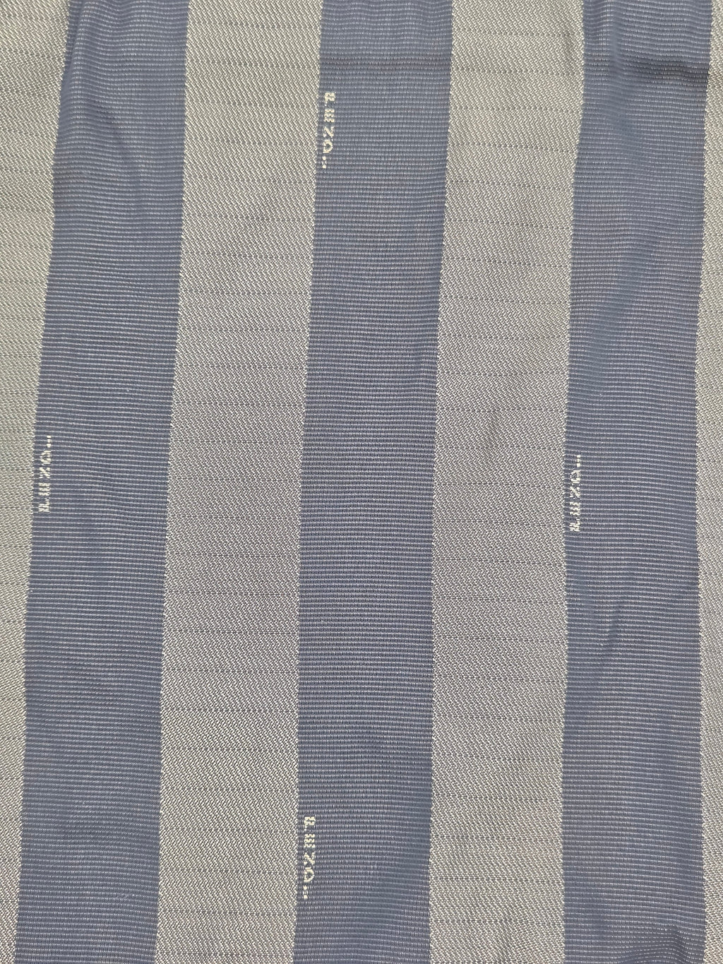 A close-up of a striped textile with alternating vertical bands of muted blue-gray and warm beige, woven with fine ribbed texture and small white printed text.