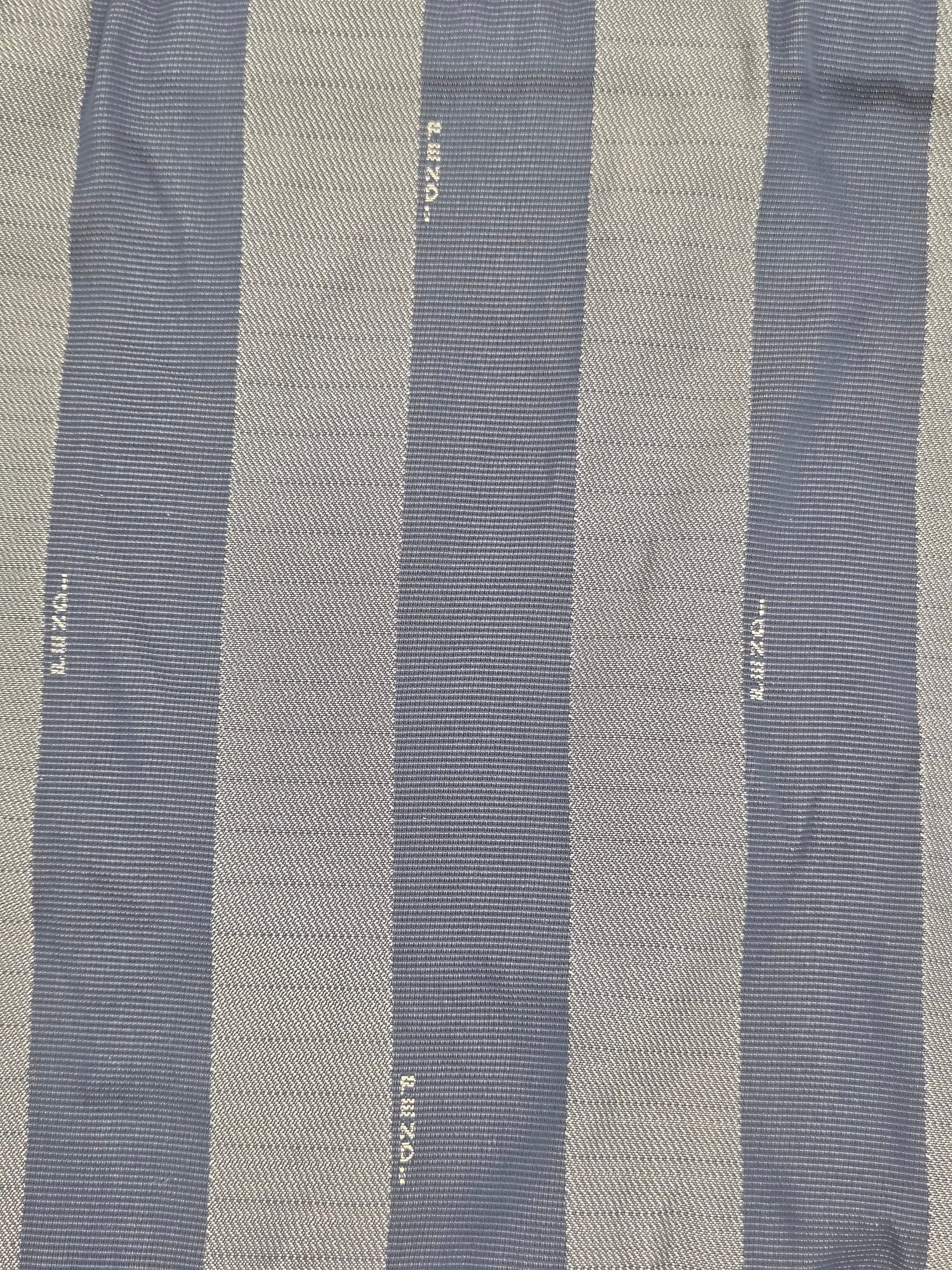 A close-up of a striped textile with alternating vertical bands of muted blue-gray and warm beige, woven with fine ribbed texture and small white printed text.