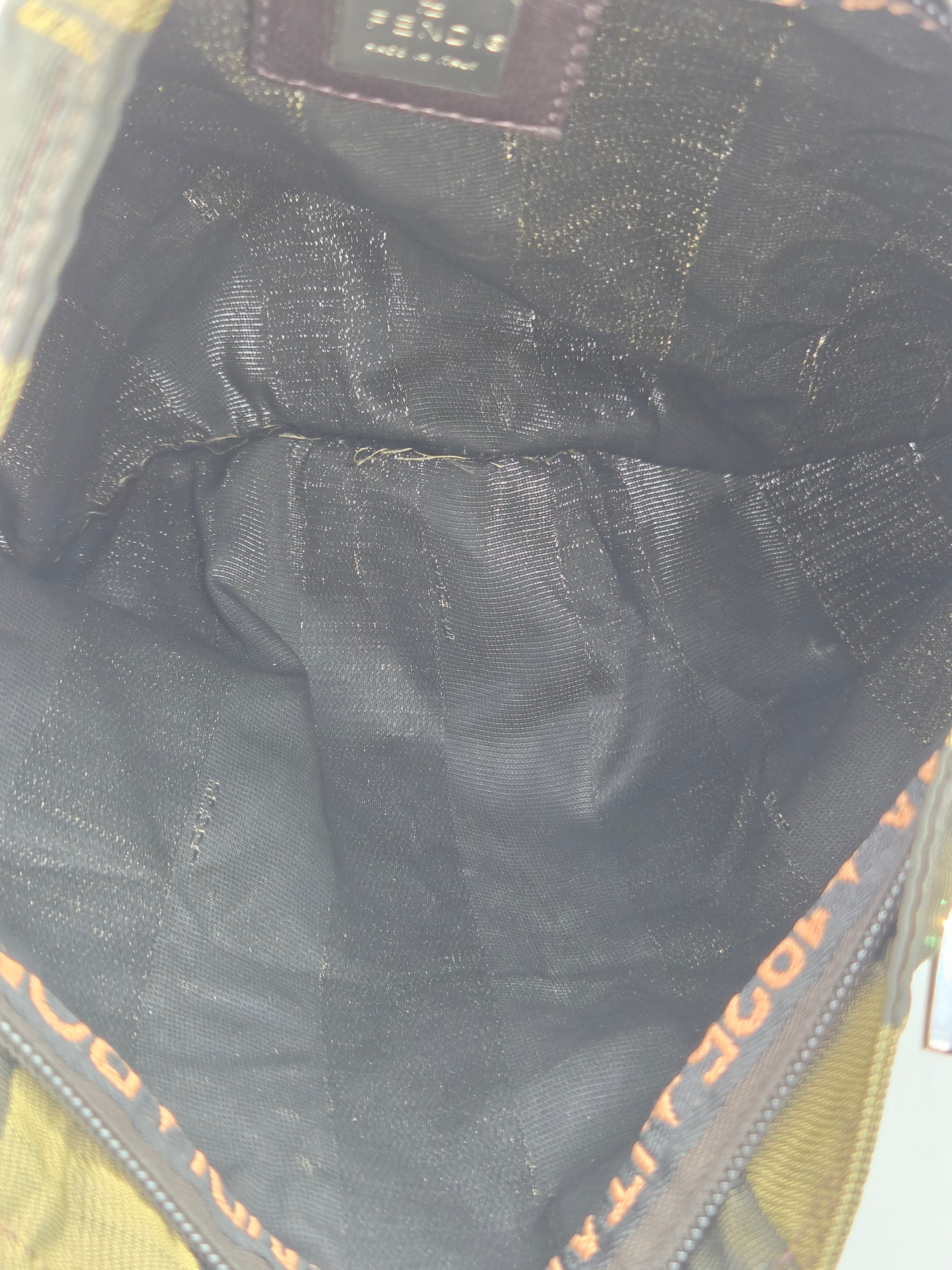 Close-up of the interior of a Fendi bag, showing a black textured fabric lining with a brown Fendi logo patch at the top and orange lettering along the zipper trim.