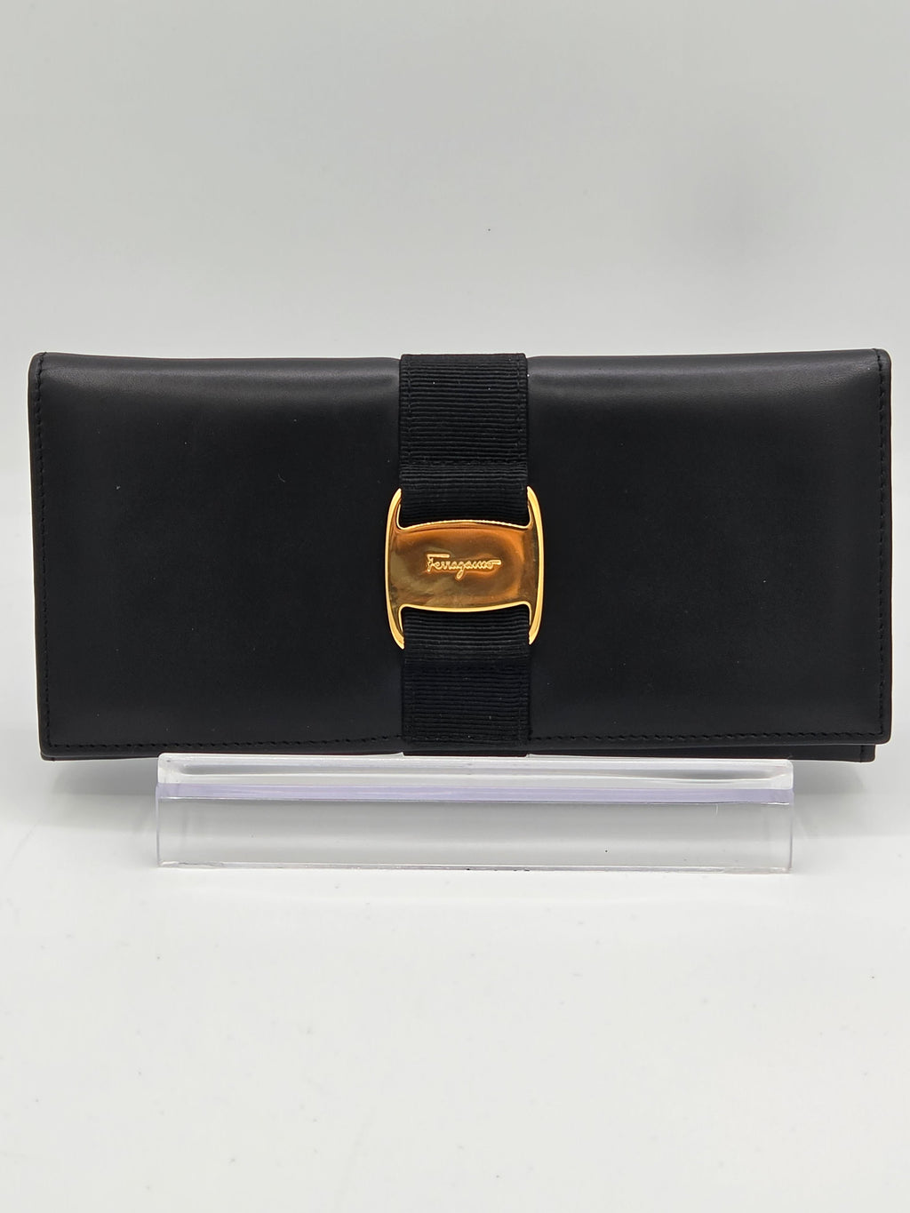 A black leather wallet with a black elastic band and a gold-tone buckle featuring the embossed Savile logo, shown next to a clear plastic protective sleeve on a white background.