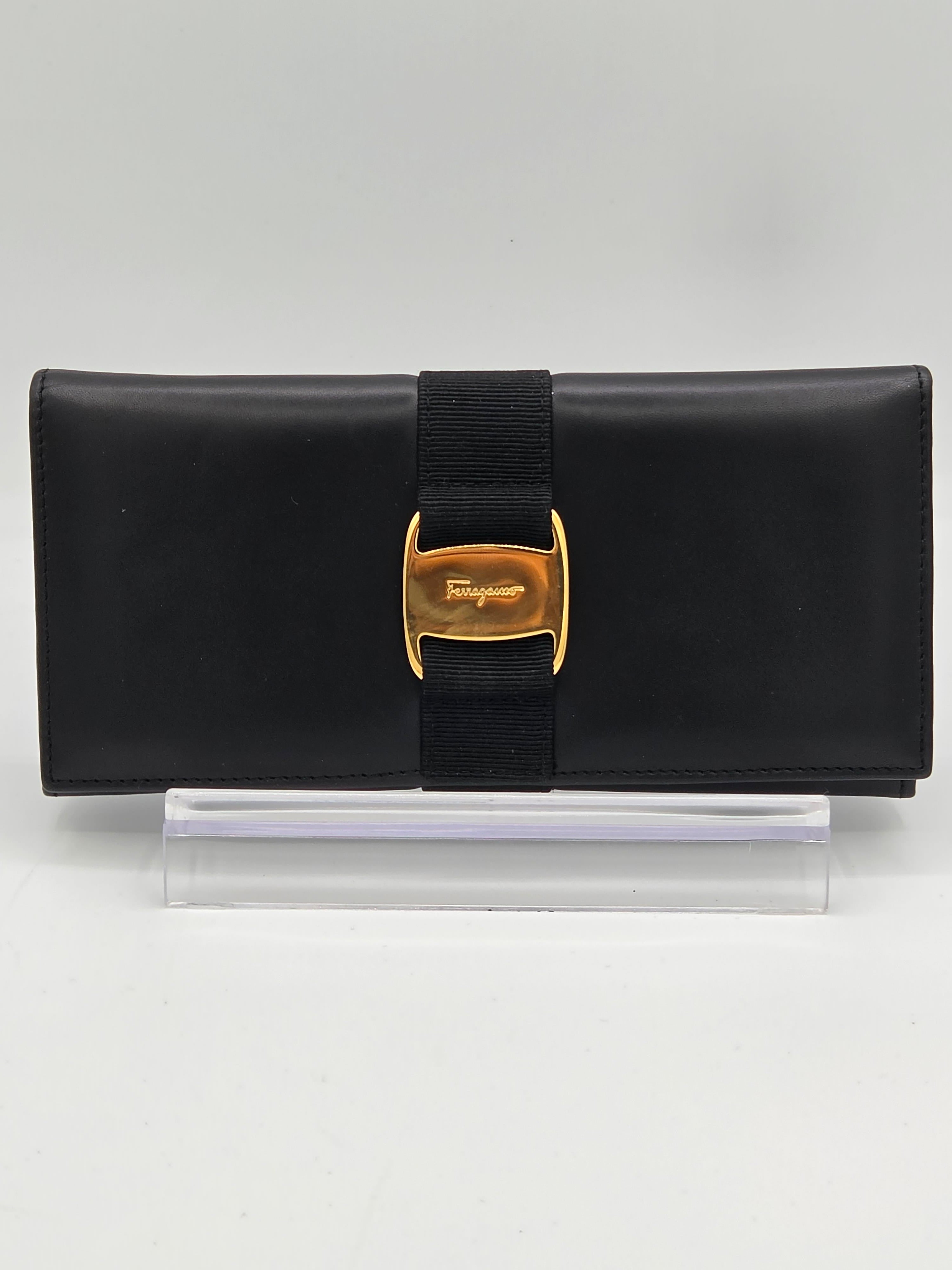 A black leather wallet with a black elastic band and a gold-tone buckle featuring the embossed Savile logo, shown next to a clear plastic protective sleeve on a white background.