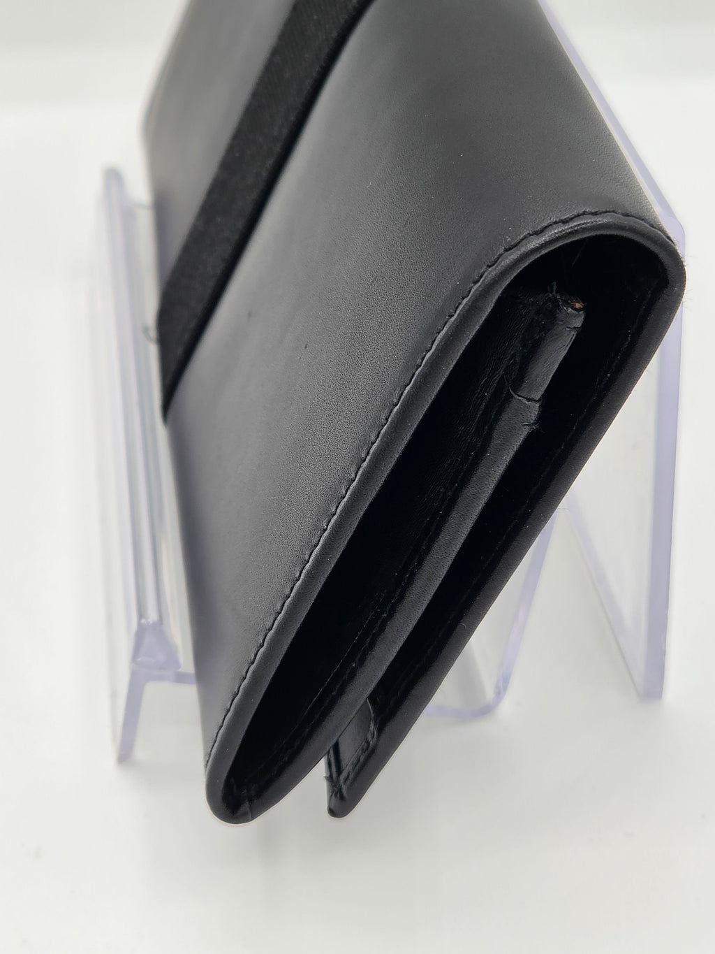 A close-up of a black leather wallet or card holder standing on a clear acrylic display stand against a white background.