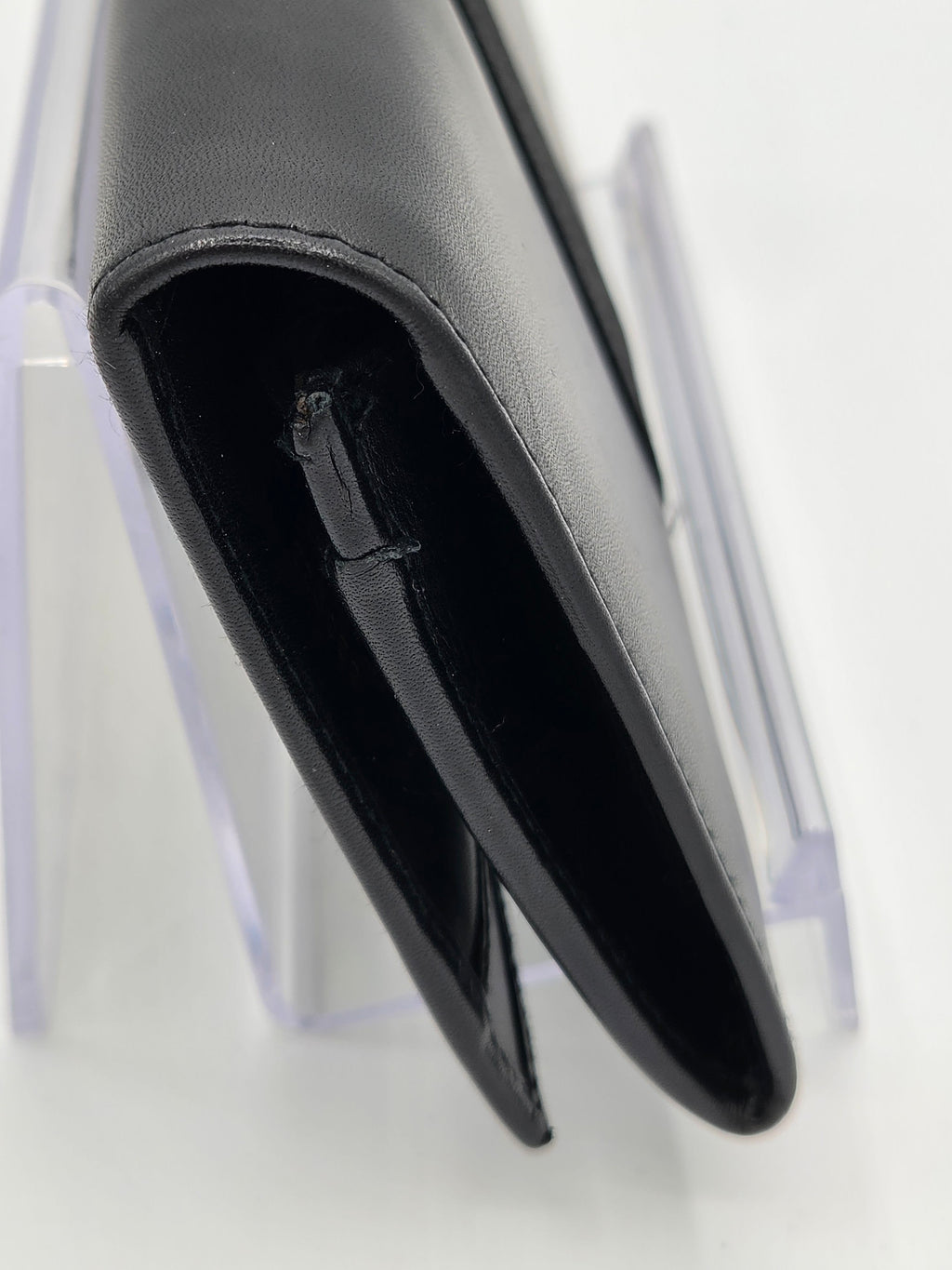 A close-up of a black leather wallet or card holder standing on a clear acrylic display stand against a white background.
