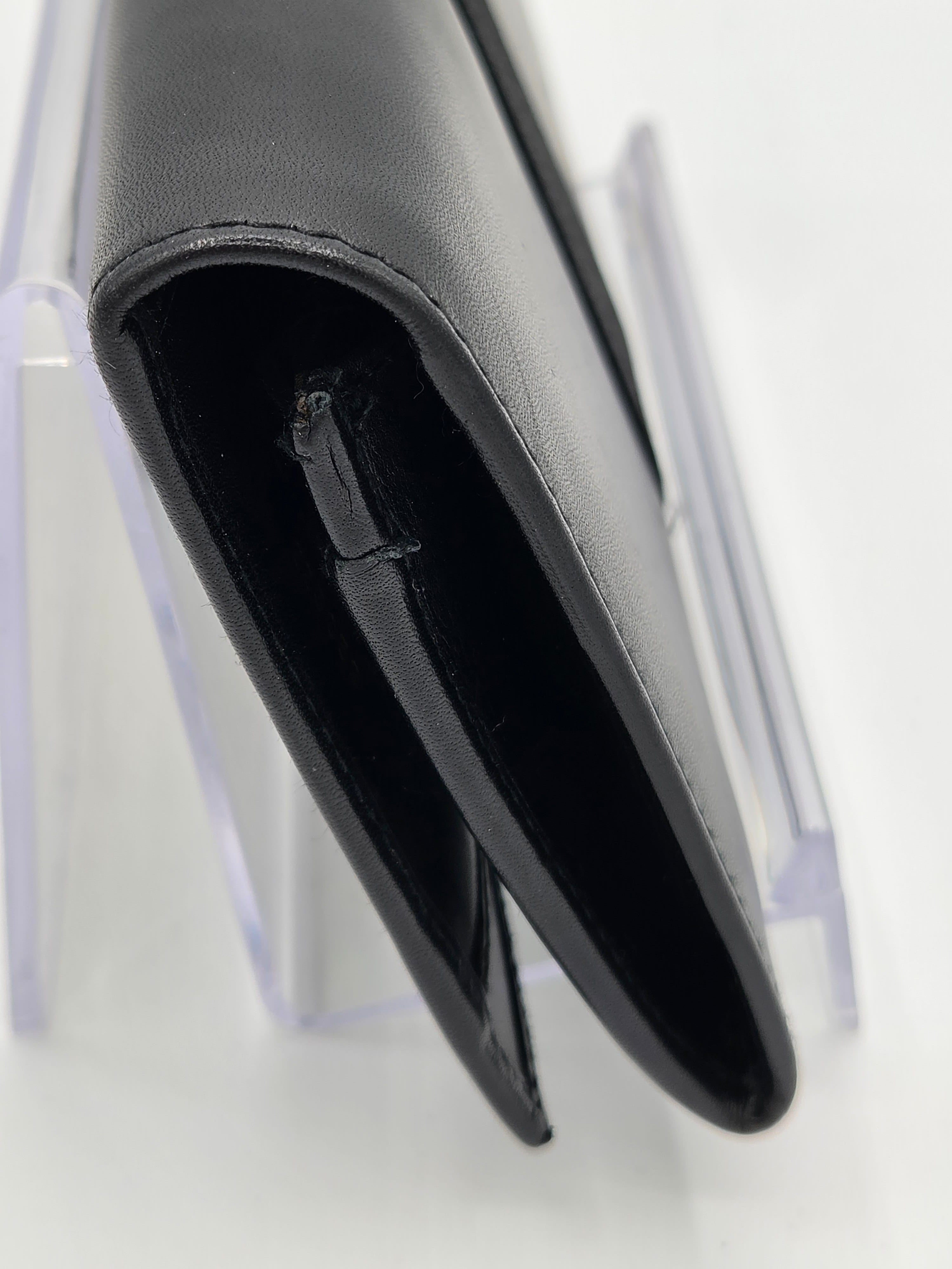 A close-up of a black leather wallet or card holder standing on a clear acrylic display stand against a white background.