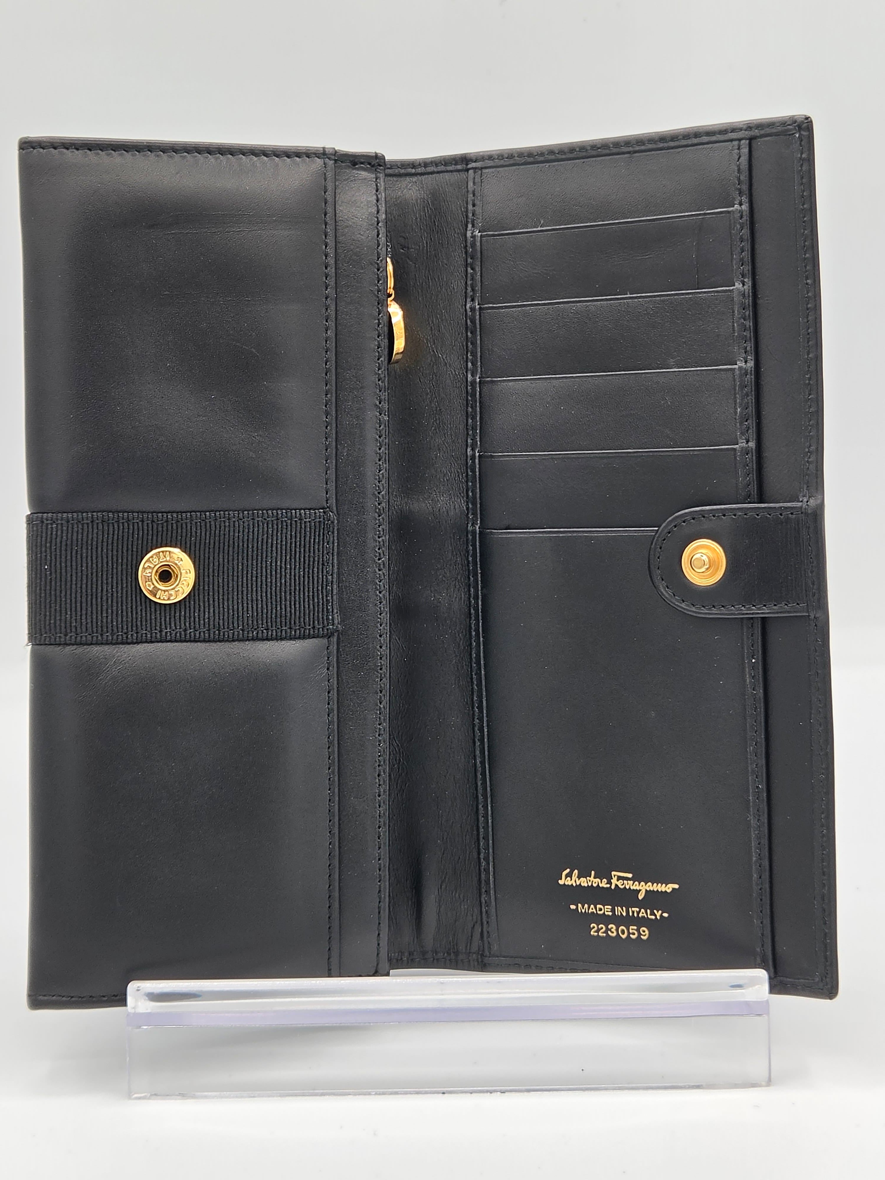 A black leather long wallet shown open, featuring multiple card slots, a zippered pocket, a central elastic band with snap buttons, and gold-tone branding on the interior.