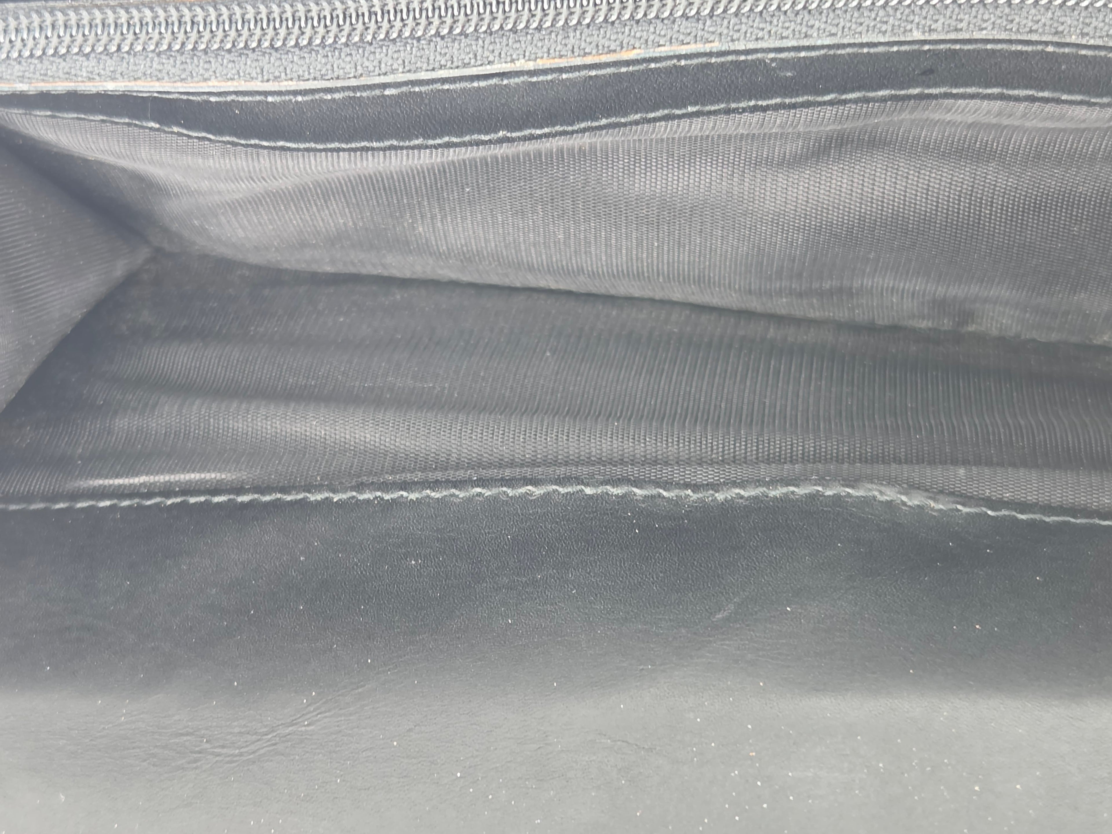 Close-up of the interior of a dark gray or black leather and fabric bag, showing stitched compartments and a zipper.