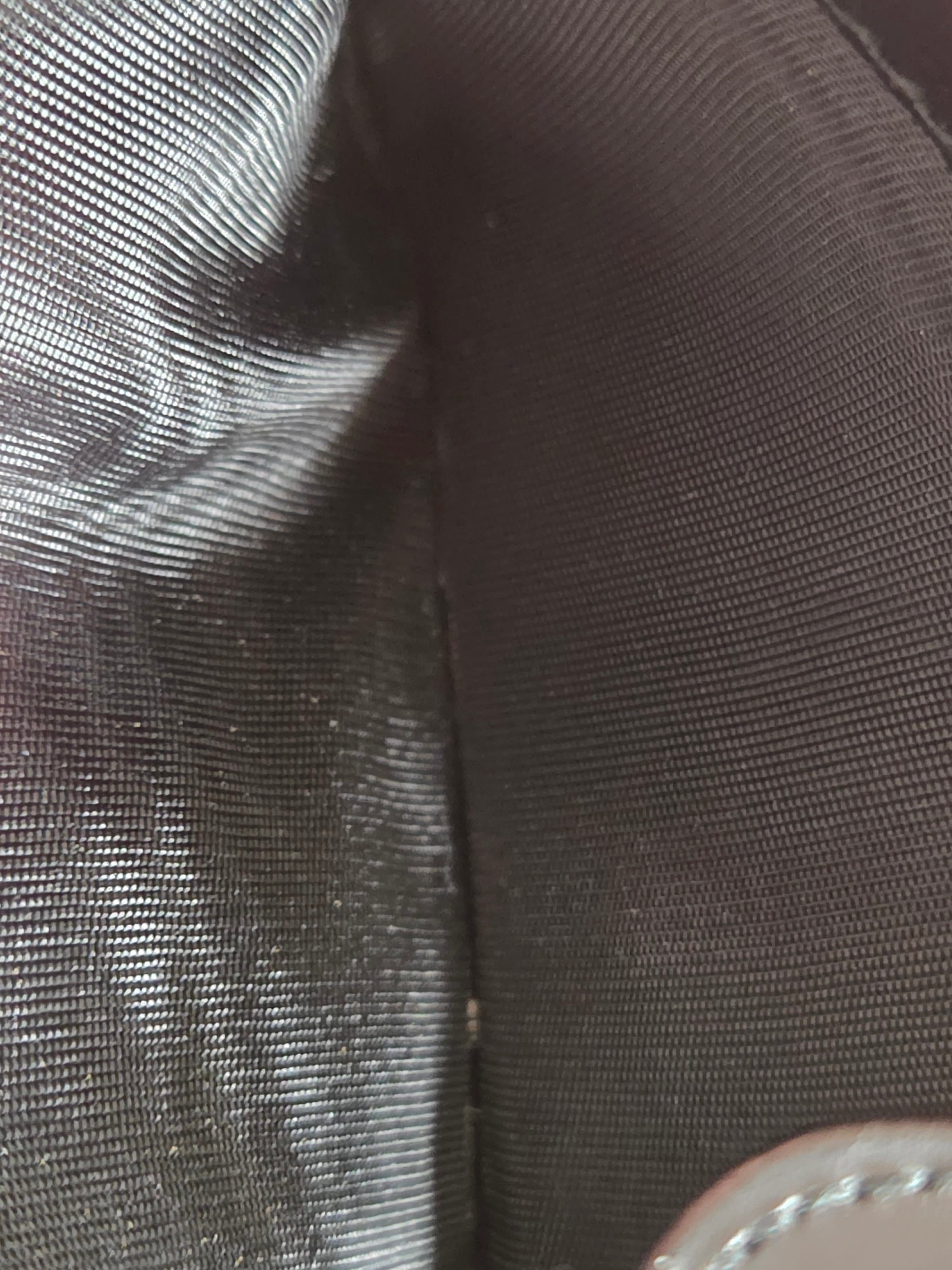 Close-up of a dark gray or black textured fabric surface with a small portion of a light-colored stitched circular detail visible in the upper right corner.