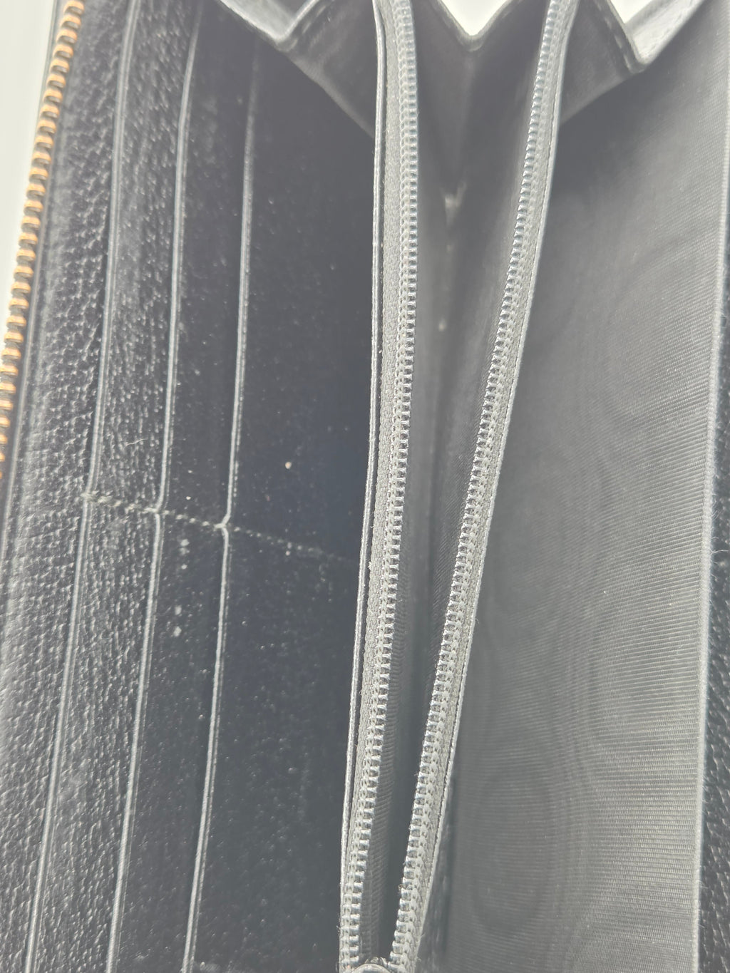 Close-up of the interior of a black leather wallet or card holder, showing multiple card slots, a zip compartment, and a subtle embossed monogram pattern on the lining.