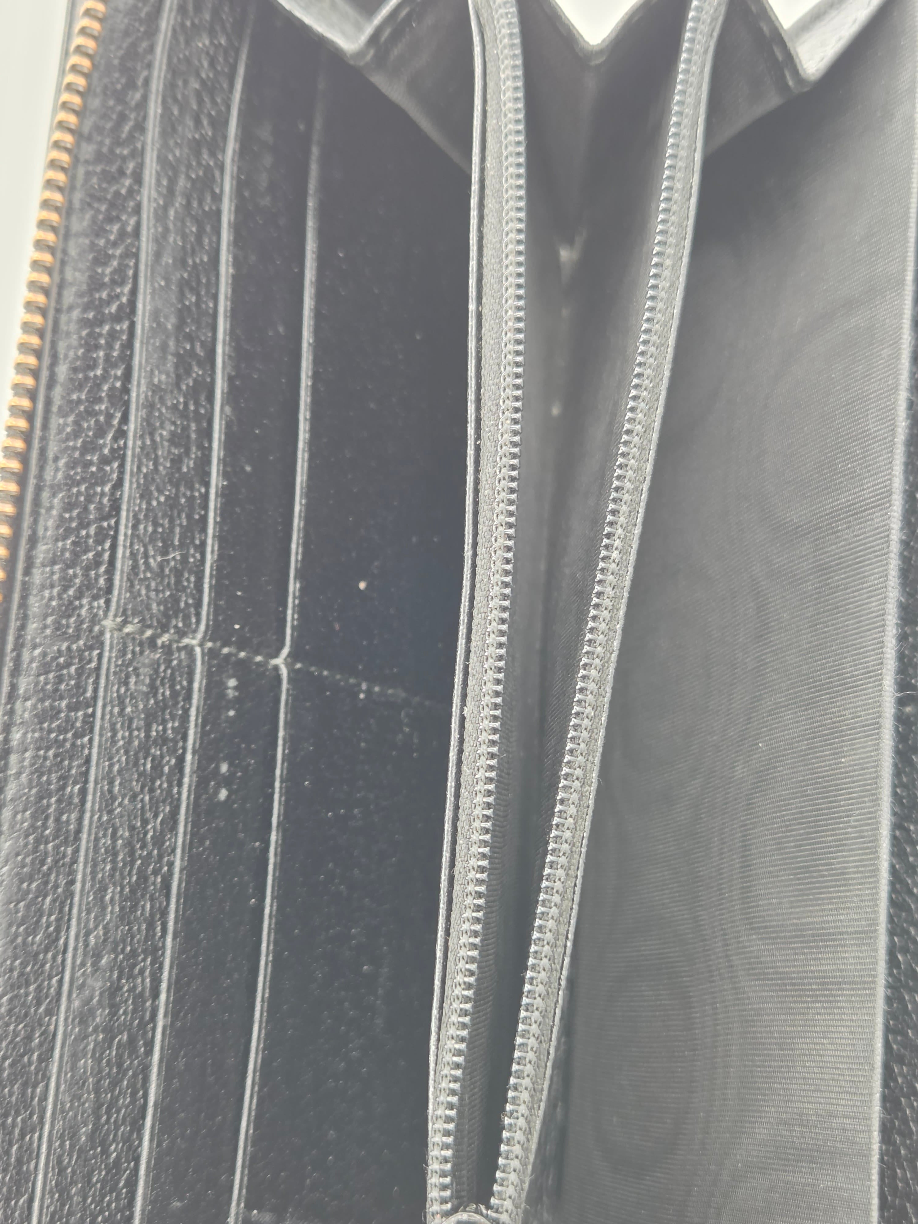 Close-up of the interior of a black leather wallet or card holder, showing multiple card slots, a zip compartment, and a subtle embossed monogram pattern on the lining.