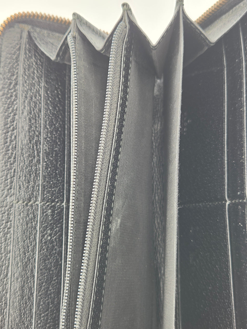 Close-up of the interior of a black leather wallet or card holder, showing multiple compartments, card slots, and a silver zipper.