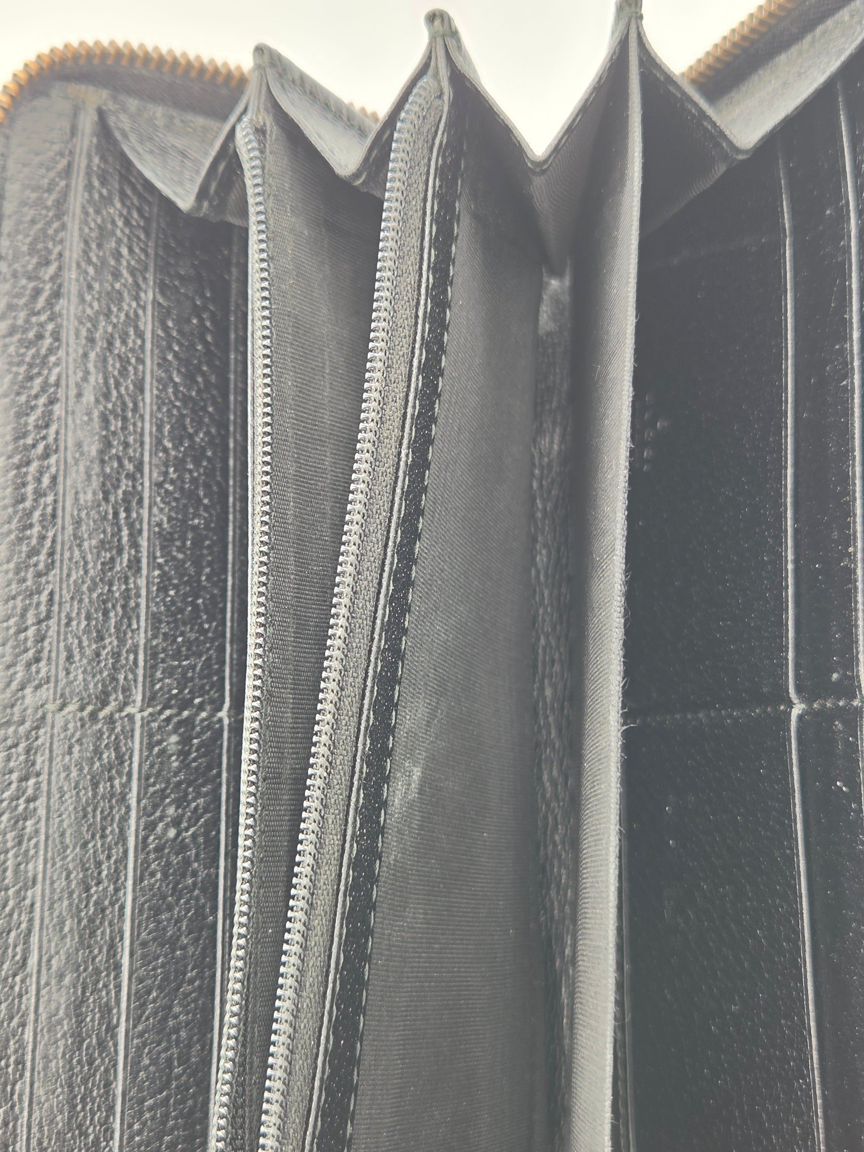 Close-up of the interior of a black leather wallet or card holder, showing multiple compartments, card slots, and a silver zipper.