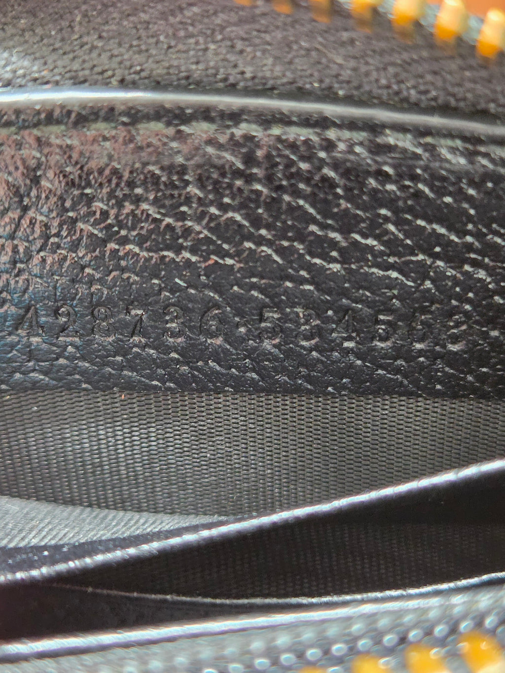 Close-up of a black textured leather or faux-leather material with a gray woven strap and a hint of yellow zipper teeth at the edges.
