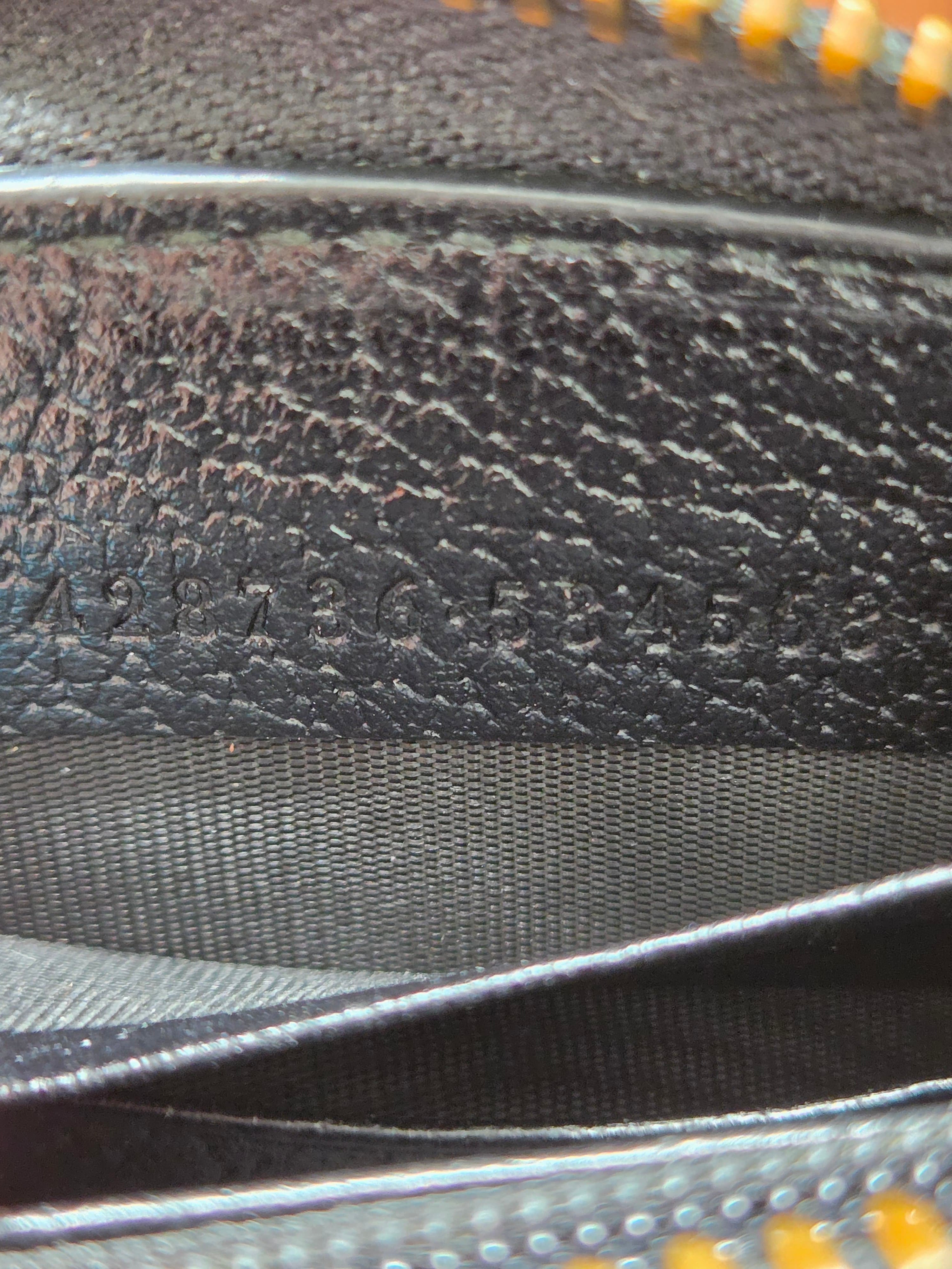Close-up of a black textured leather or faux-leather material with a gray woven strap and a hint of yellow zipper teeth at the edges.