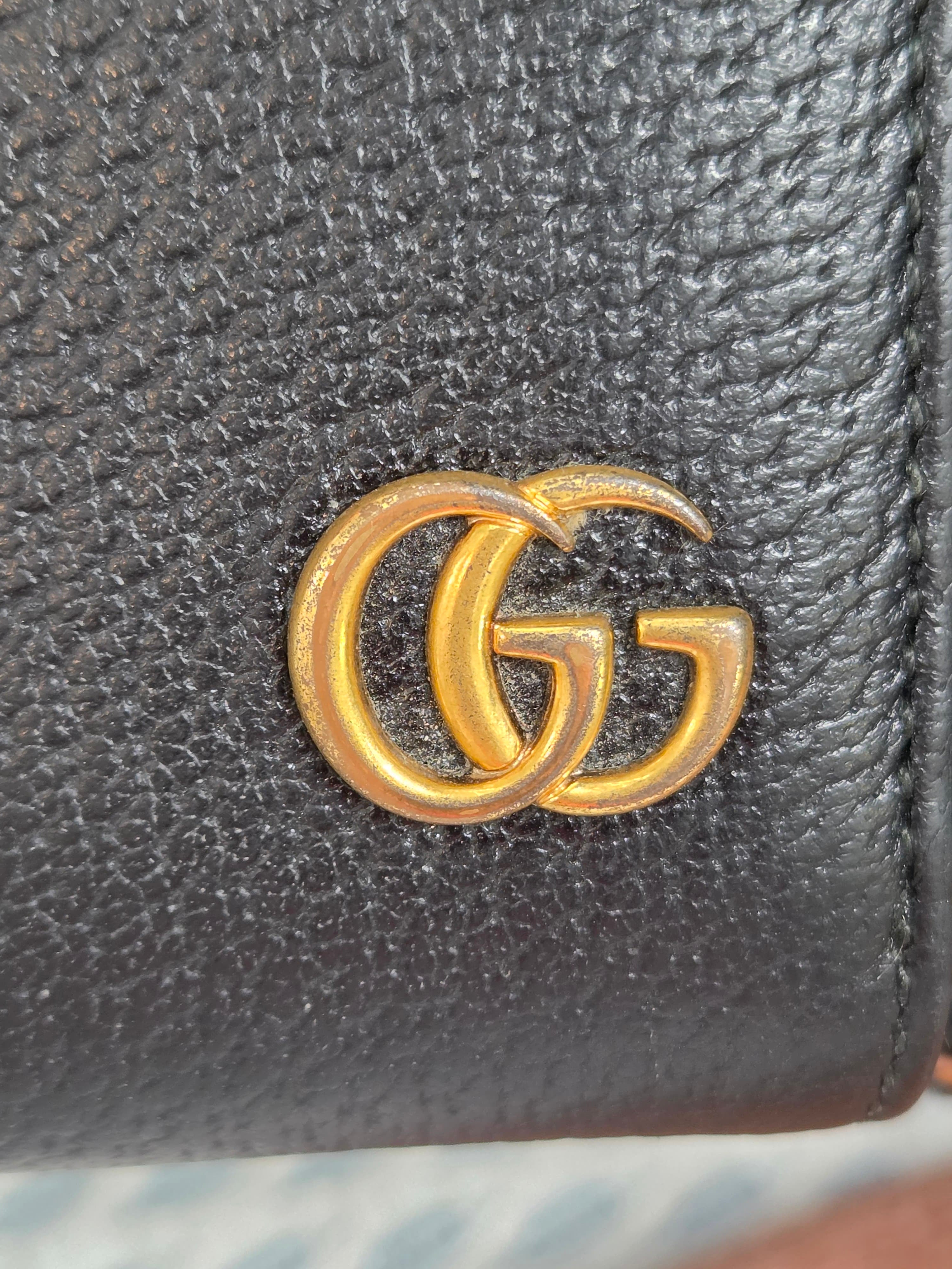 Close-up of a black pebbled leather item featuring a prominent gold interlocking G logo emblem, characteristic of Gucci.
