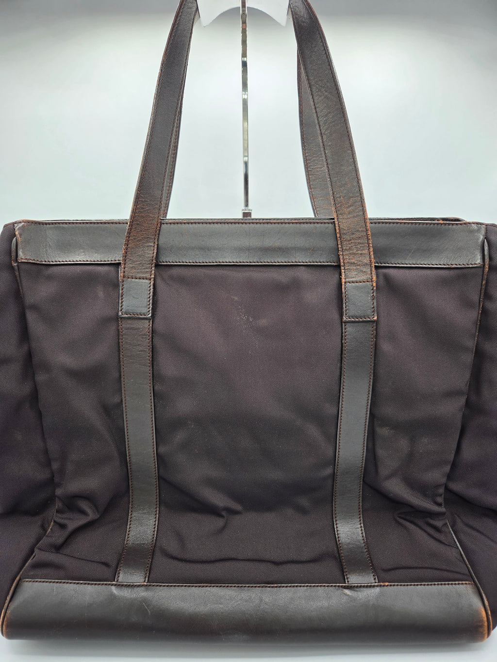 A dark brown canvas tote bag with dark brown leather shoulder straps and trim, shown from a top-down angle against a light gray background.