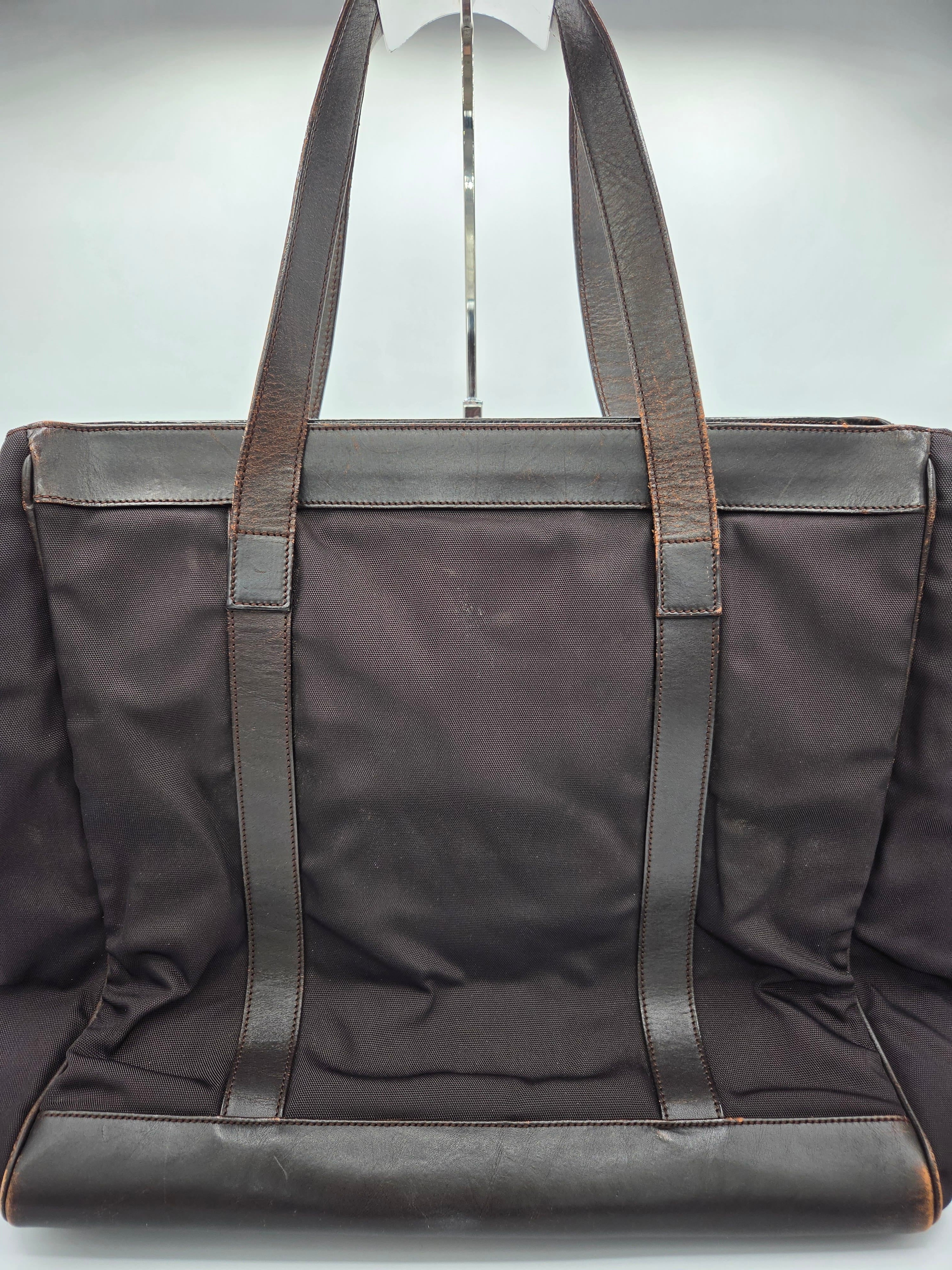 A dark brown canvas tote bag with dark brown leather shoulder straps and trim, shown from a top-down angle against a light gray background.